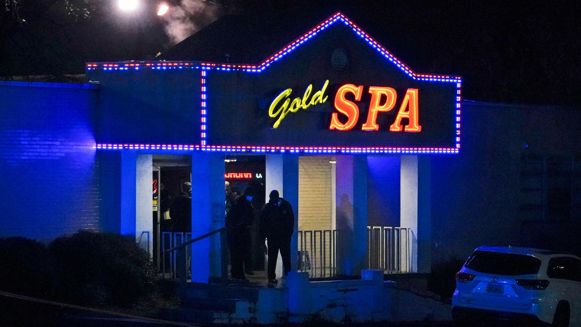 The front door of a spa is shown lit with blue colors and a sign above the entrance with the name, Gold Spa in neon lighting.