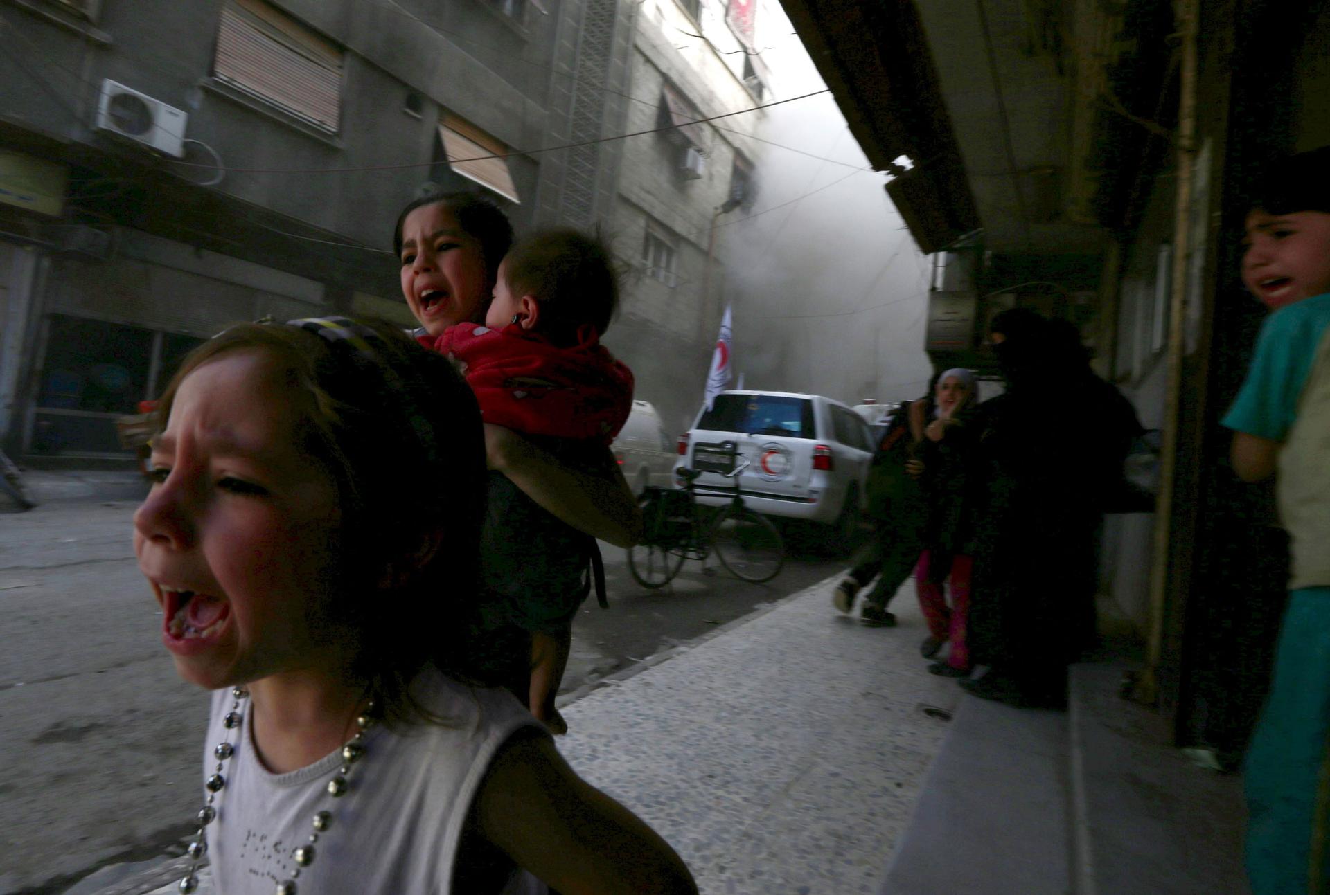 Ghazal, 4, (left) and Judy, 7, carrying 8-month-old Suhair, run away after the shelling of a Red Crescent convoy in Damascus, Syria, May 6, 2015.