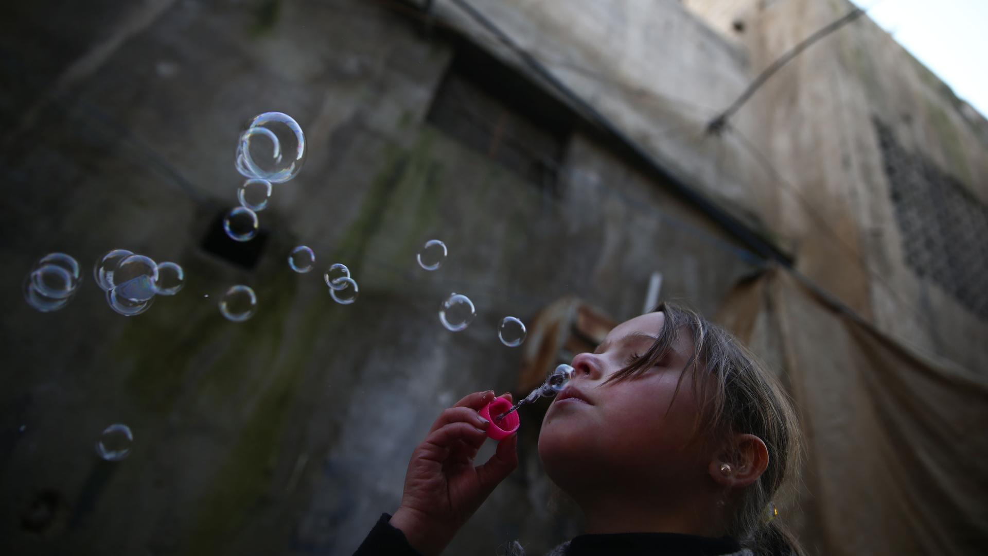 A young girl blows bubbles in the Douma neighborhood of Damascus, Syria, Jan. 19, 2017.