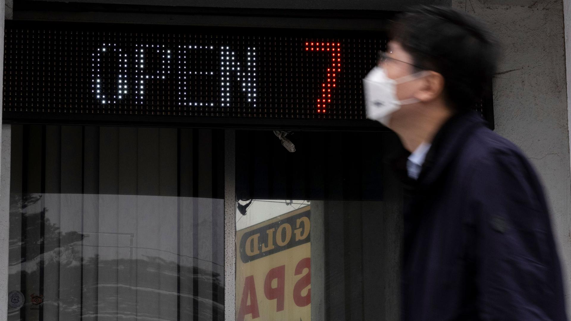 A man is shown in blurred focus walking past a digital sign that says, 'open 7' and glass beneth it with the sign for Gold Spa in the reflection.