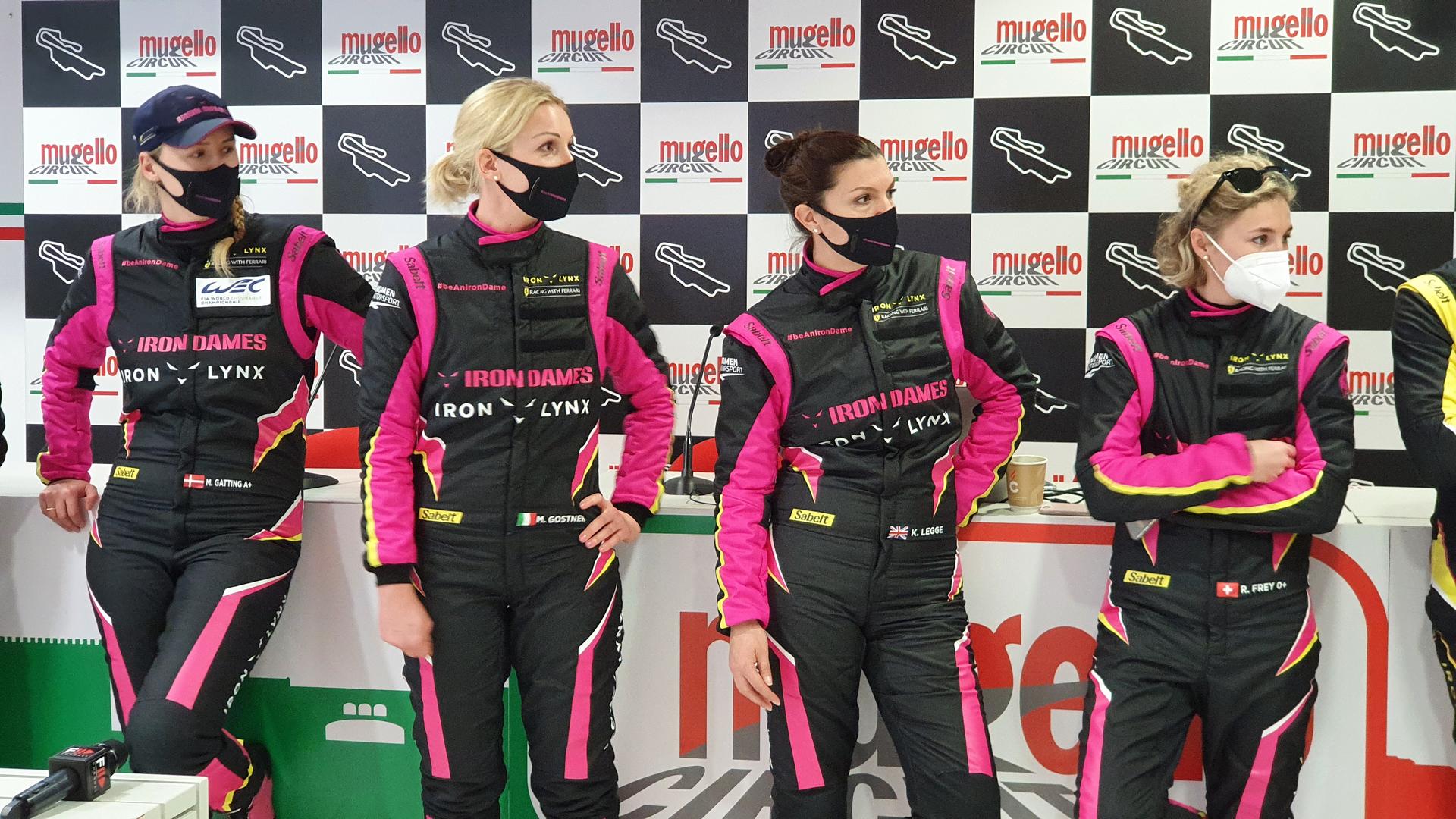Four women wear black and pink race tracksuits.
