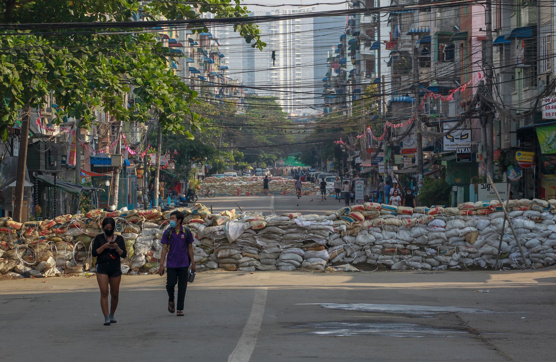 People walk along a deserted road blocked with improvised barricades build by anti-coup protesters to secure a neighborhood in Yangon, Myanmar, March 18, 2021.