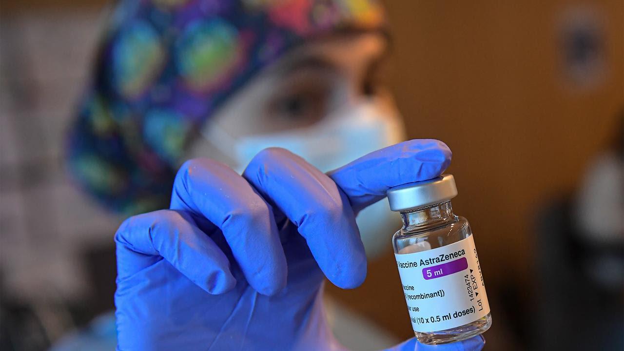 A person holds a vial of a vaccine dose wearing blue gloves