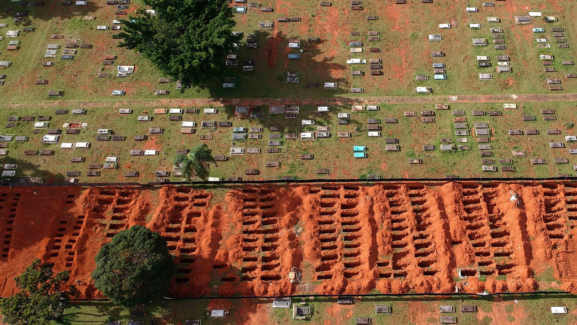 A cemetery is shown via an ariel view with several rows of empty new graves and exposed dirt.