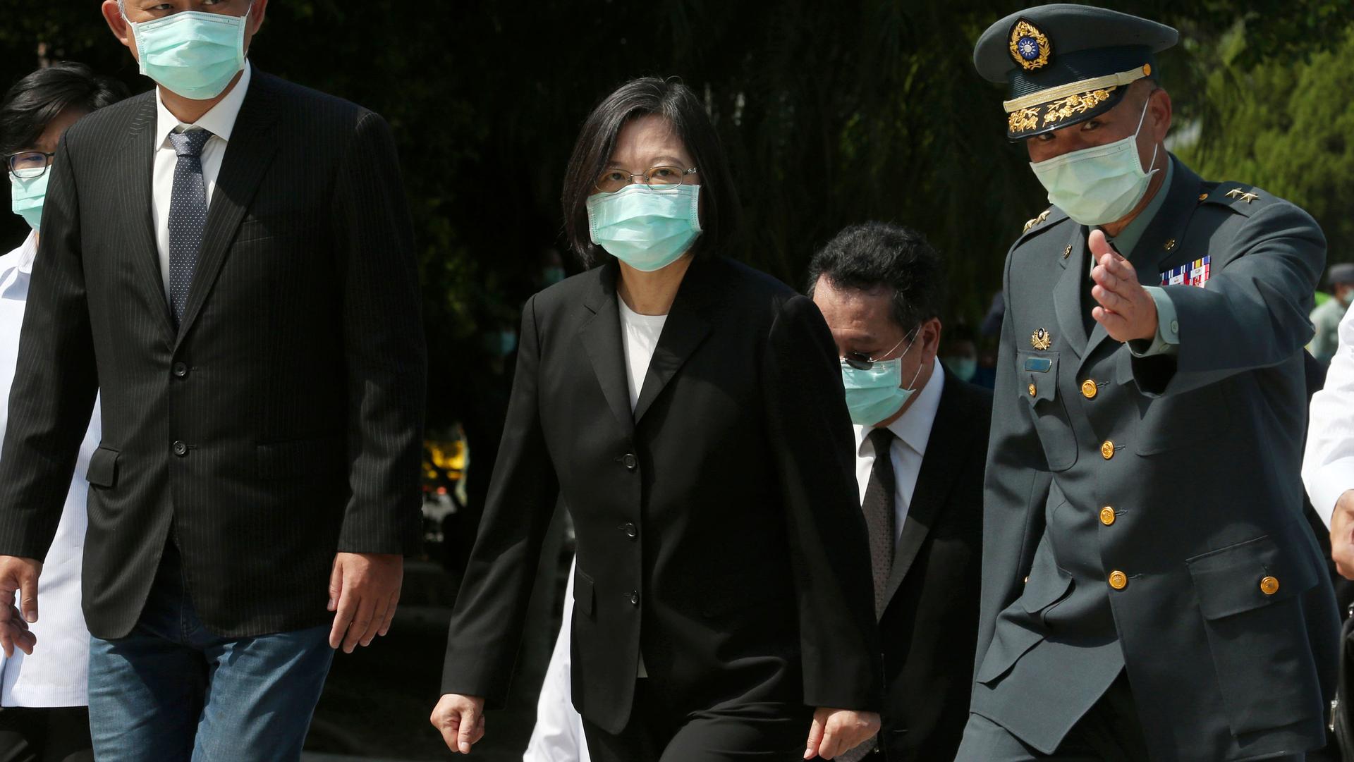 Taiwan's President Tsai Ing-wen is shown wearing a dark suit and walking while flanked by a military officials to her left.