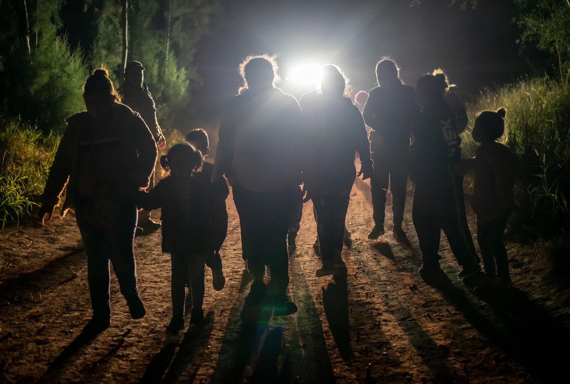 A group of noncitizens crossing the border at night, silhouetted against a light