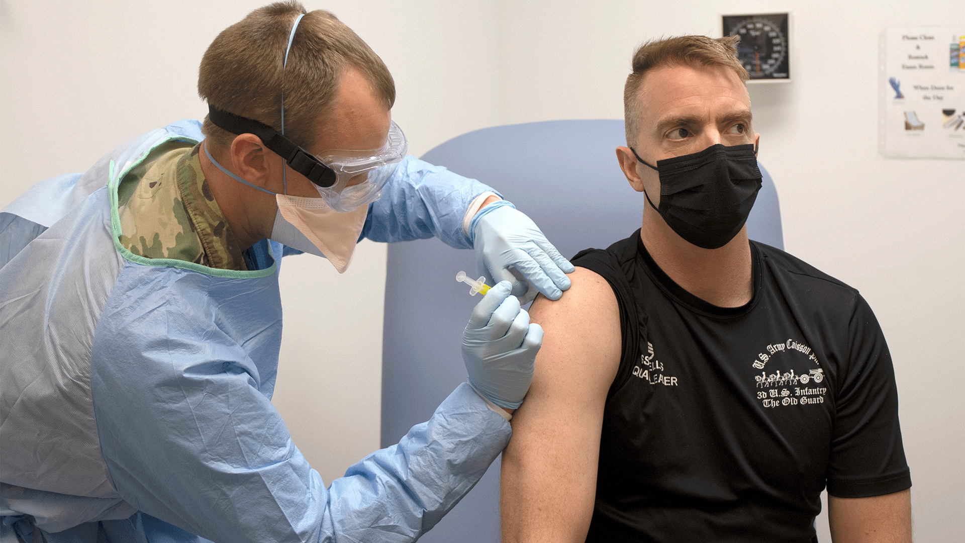 Army captain in scrubs administers COVID-19 vaccine to man in black shirt