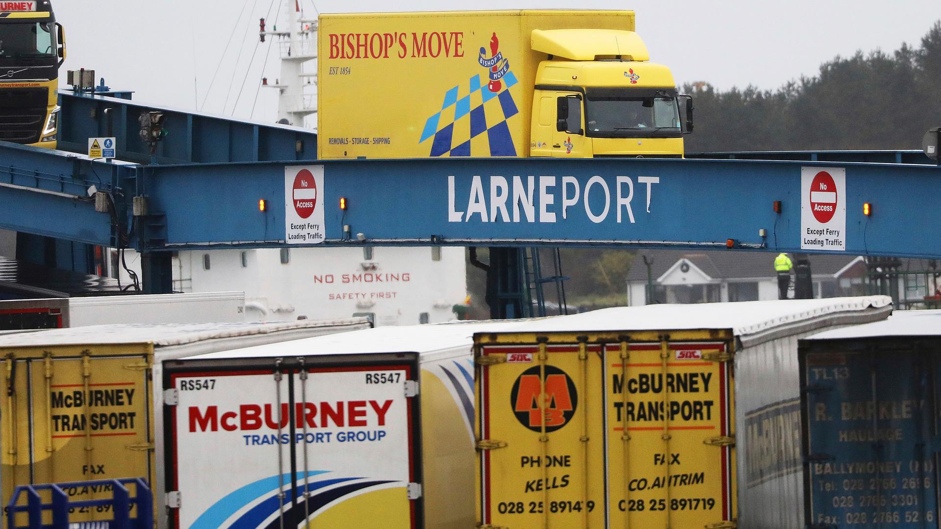 Blue, yellow, and white vehicles disembark from a ferry arriving from Scotland.  