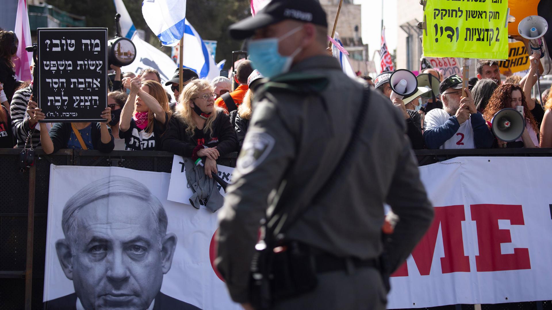 A large crowd of people are shown with several holding a banner showing Israeli Prime Minister Benjamin Netanyahu's face.