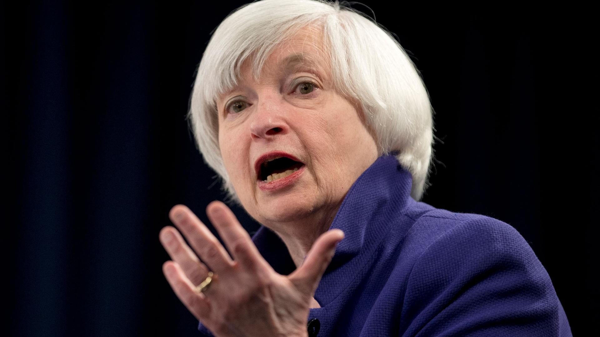 Janet Yellen is shown in a close up photograph speaking with her left hand raised palm up.