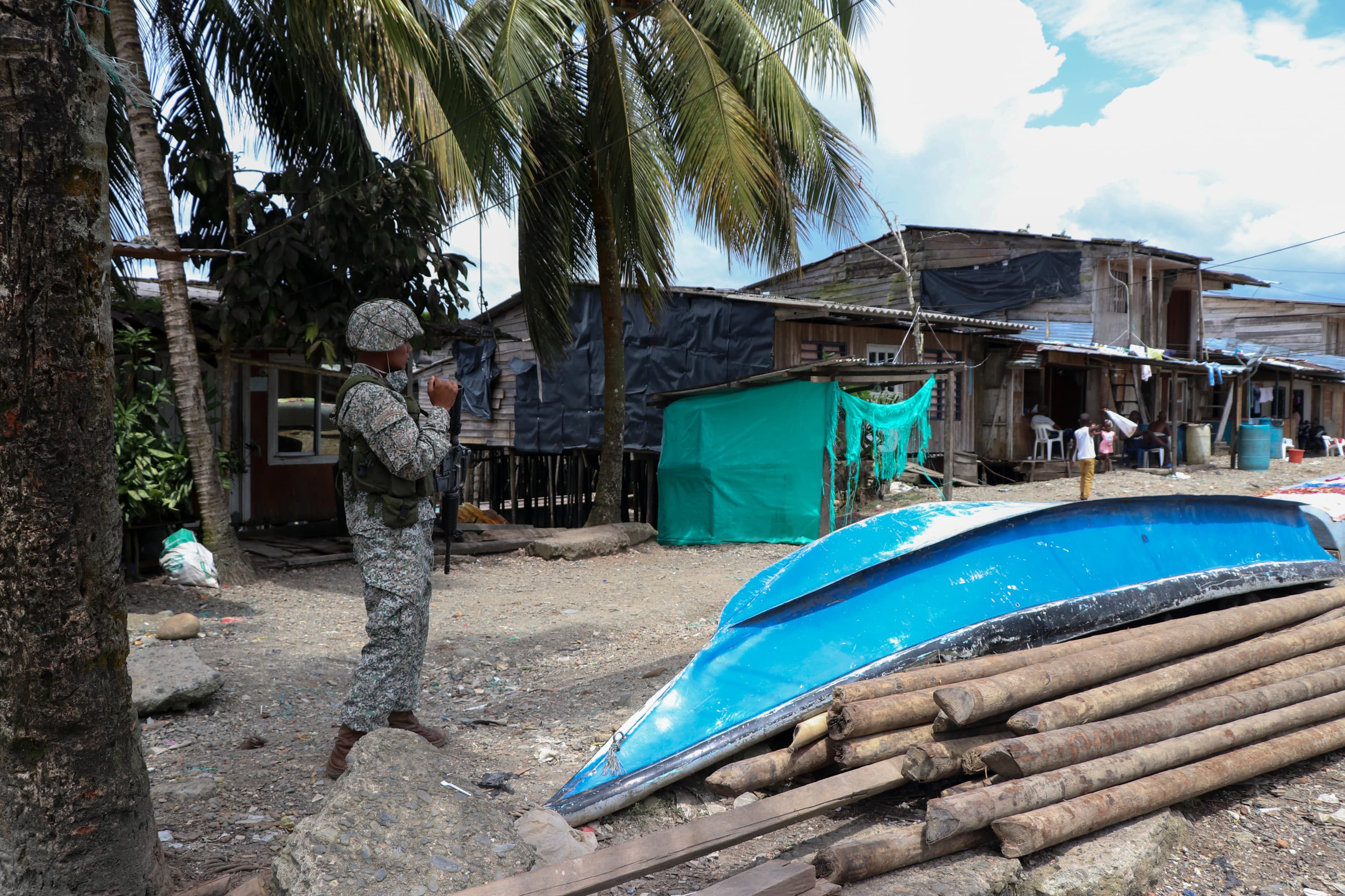 A soldier on patrol in a neighborhood with a boat on the street.