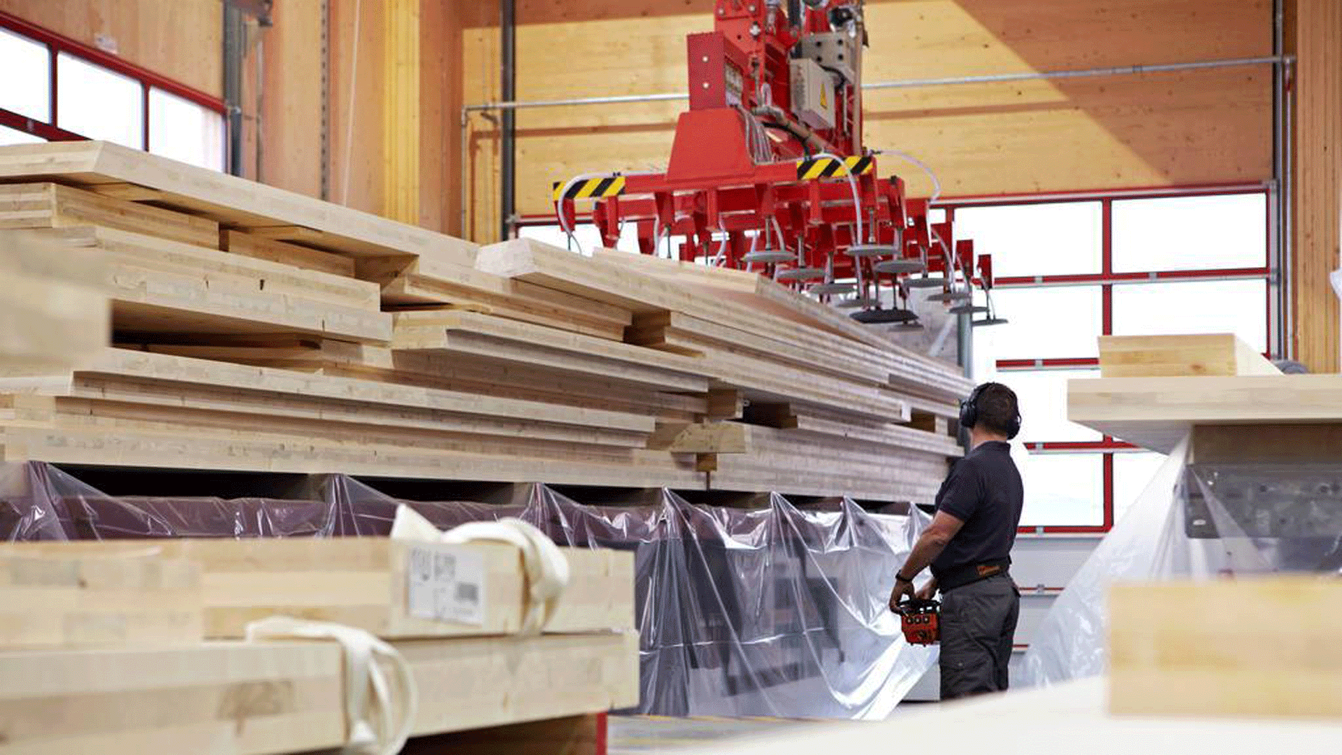 A man stand next to a machine with large slabs of wood.