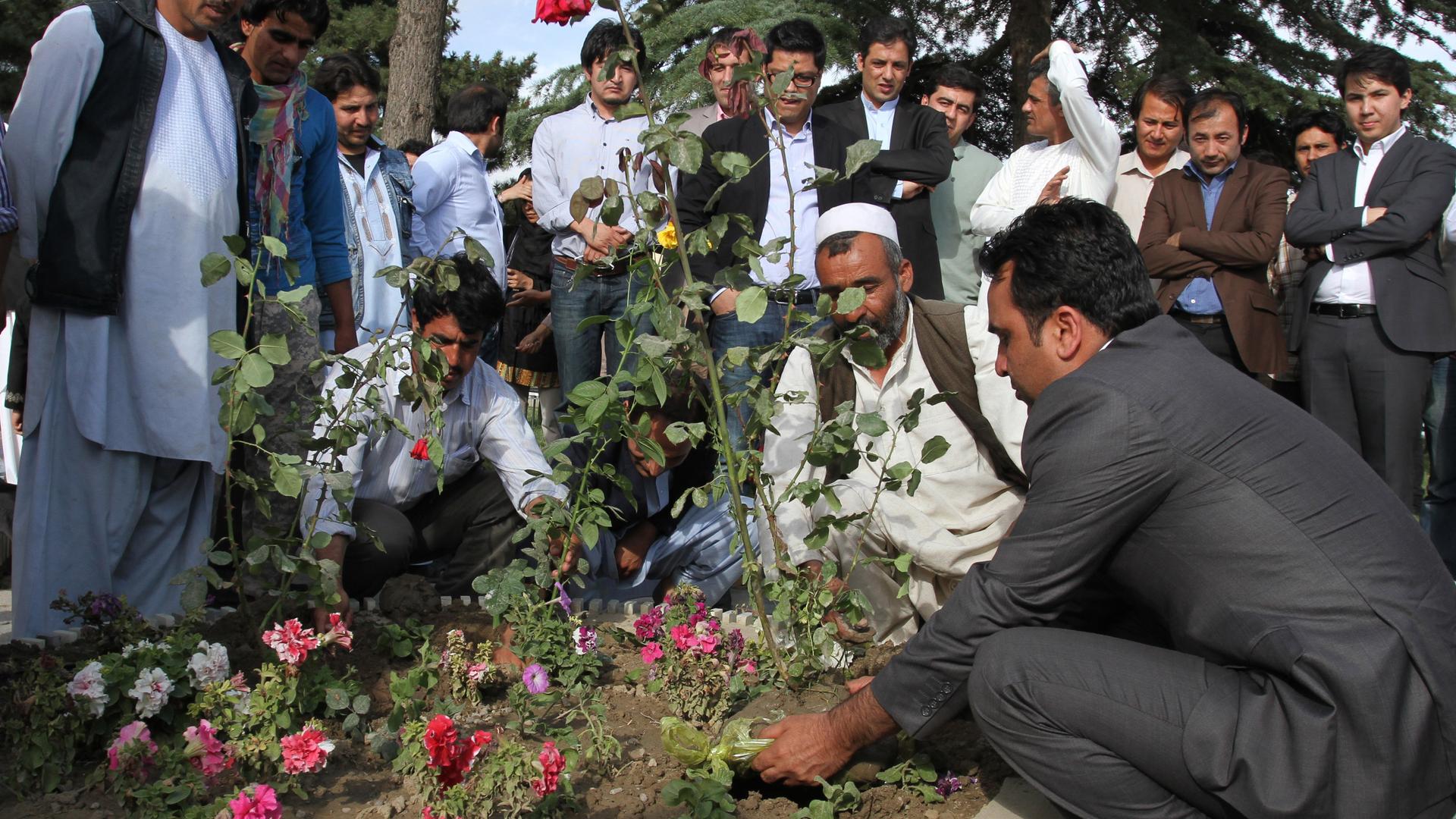 A group of men gather around a memorial to plant flowers for victims of a militant attack.
