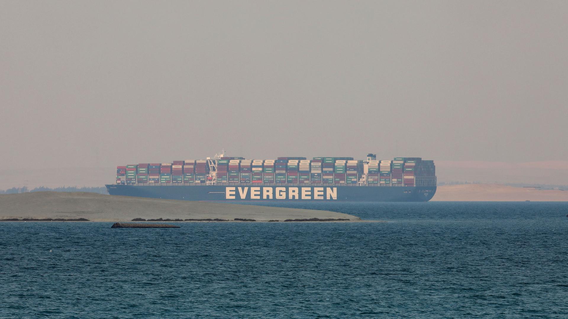 The massive cargo ship, the Ever Given, is shown in the watery distance stacked with containers.