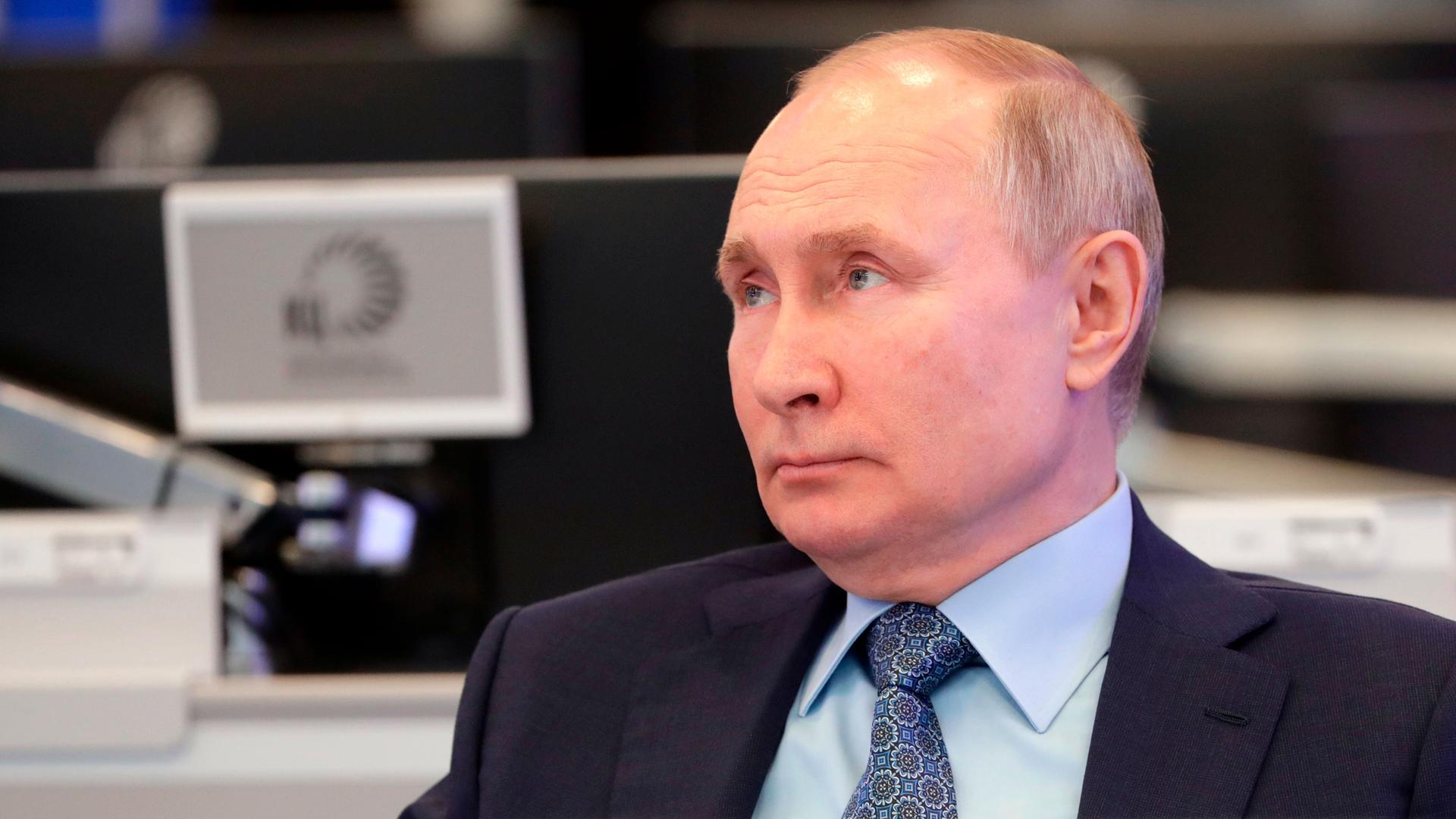 Russian President Vladimir Putin is shown in a close-up photograph wearing a dark suit and tie and looking off to his right.