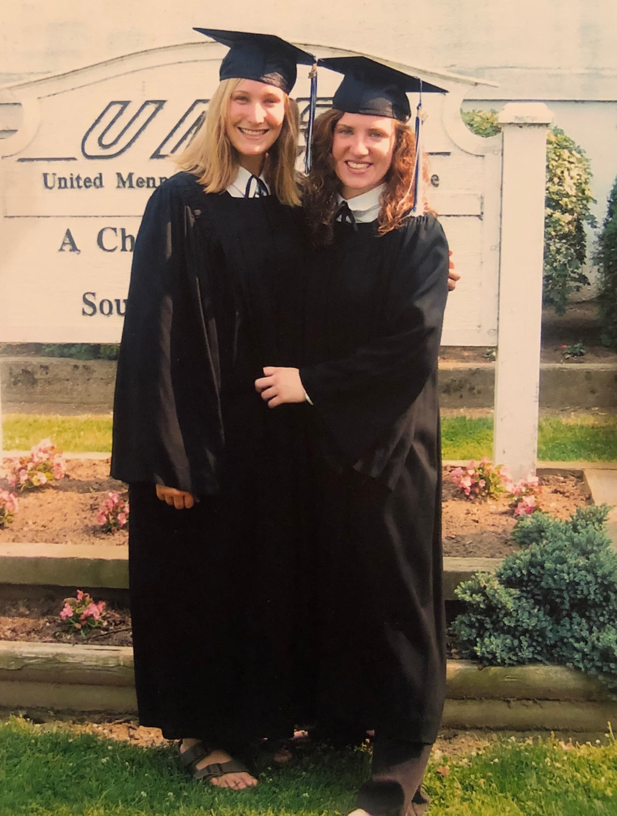Two young women wear graduation robes and caps and stand close for a photo.