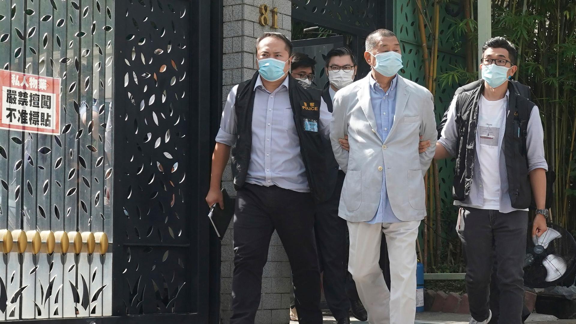 Hong Kong media tycoon Jimmy Lai, is shown wearing a light colored blazer with his hands handcuffed behind his back.