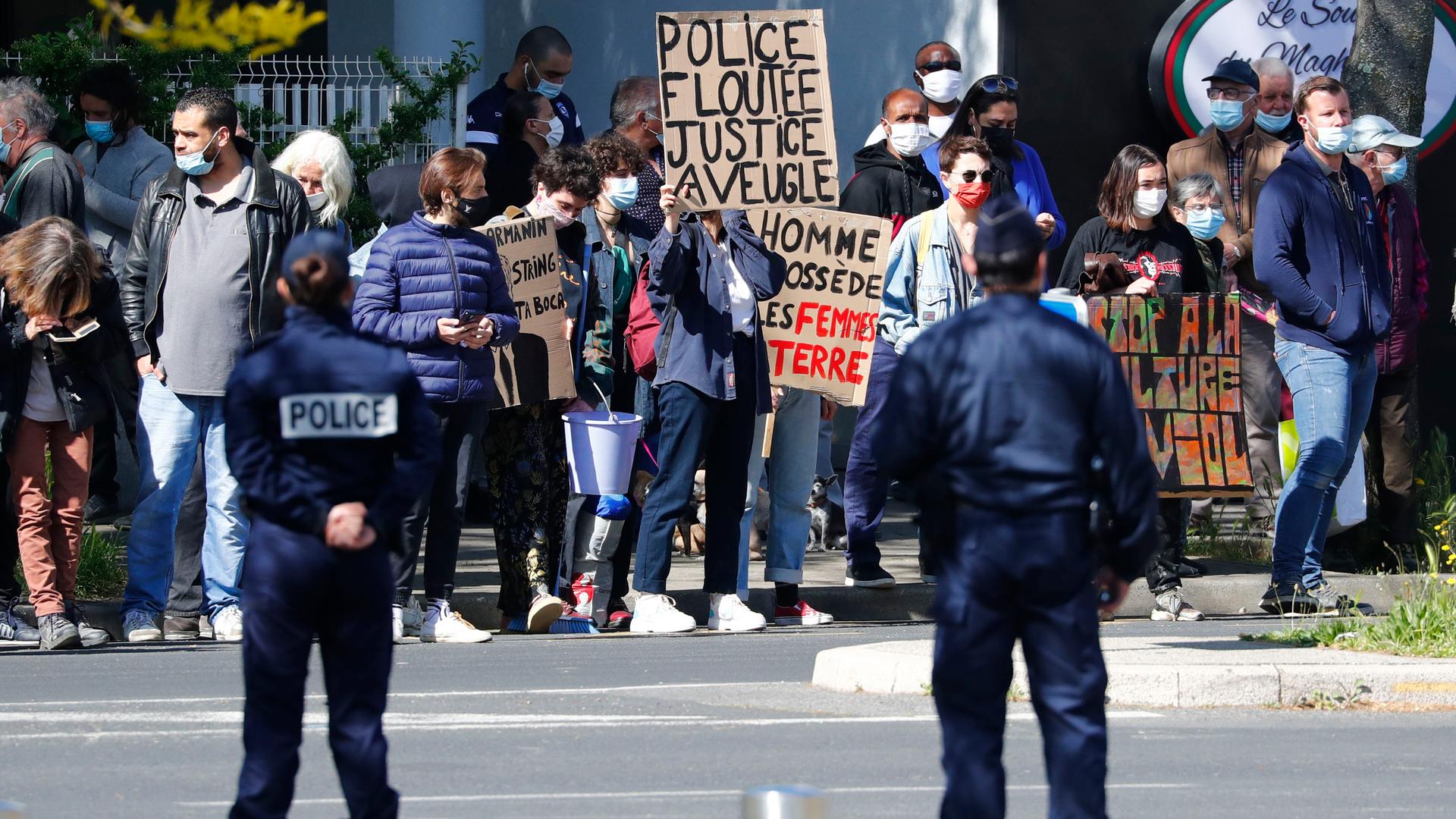 Two uniformed police stand before a crowd of protesters holding banners and signs