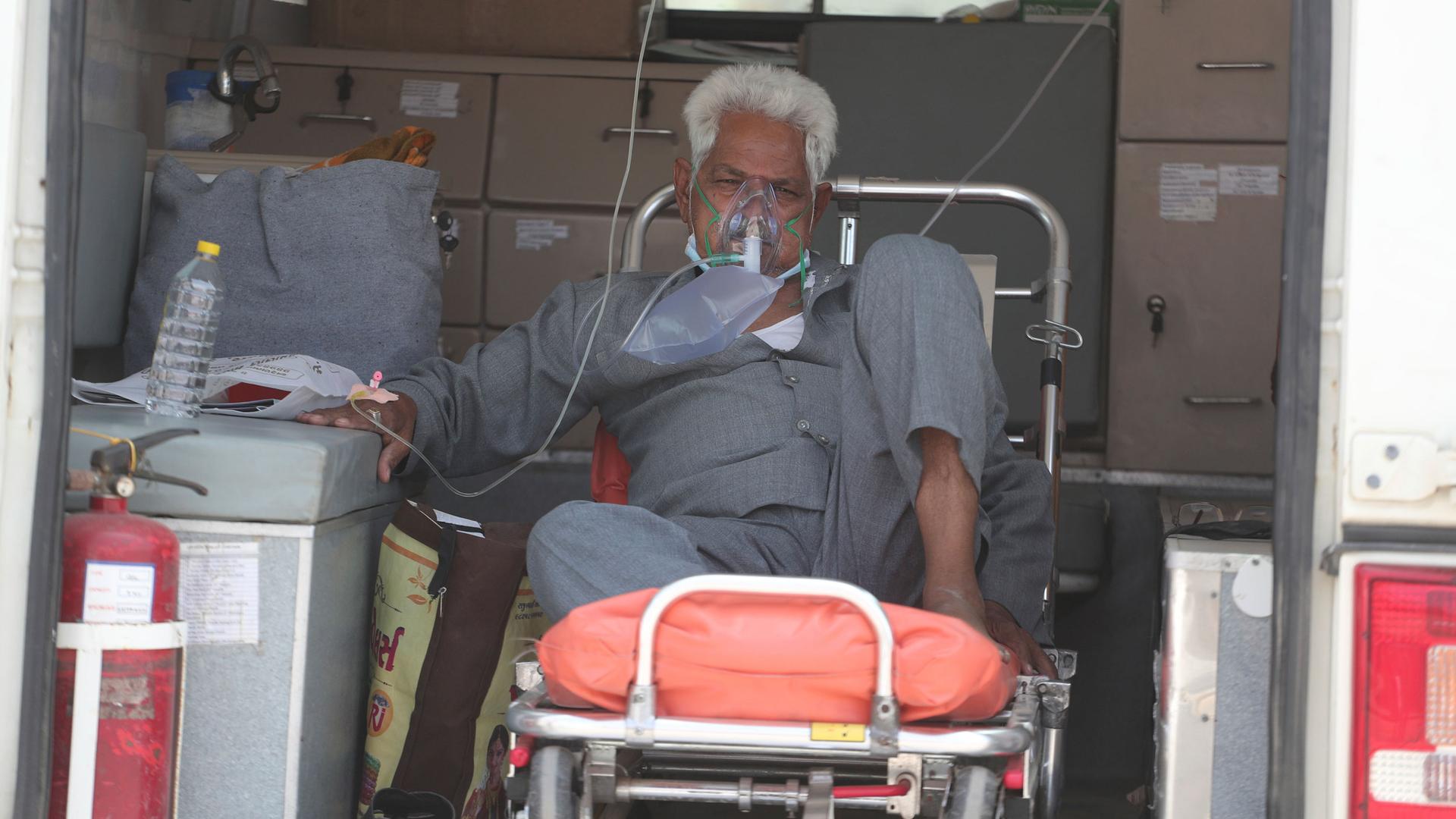 An older man is shown sitting on a gurney with a face mask on supplying oxygen.