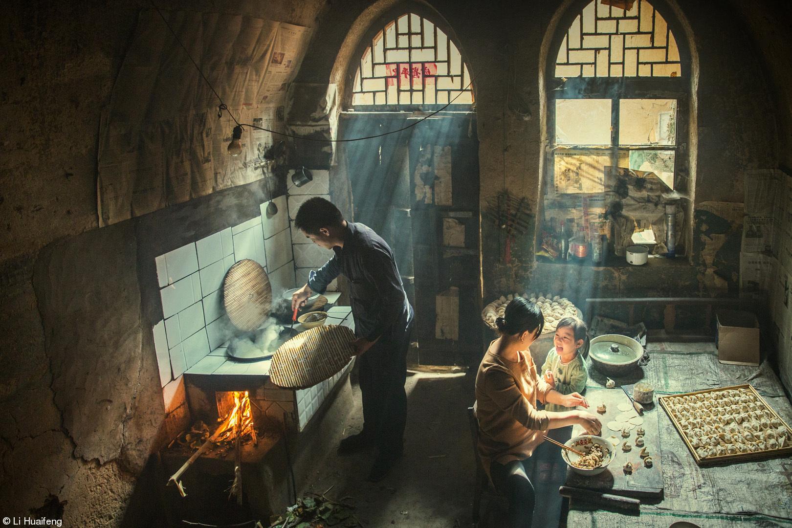 A man is shown tending to cooking with a woman behind him preparing good next to a young child.