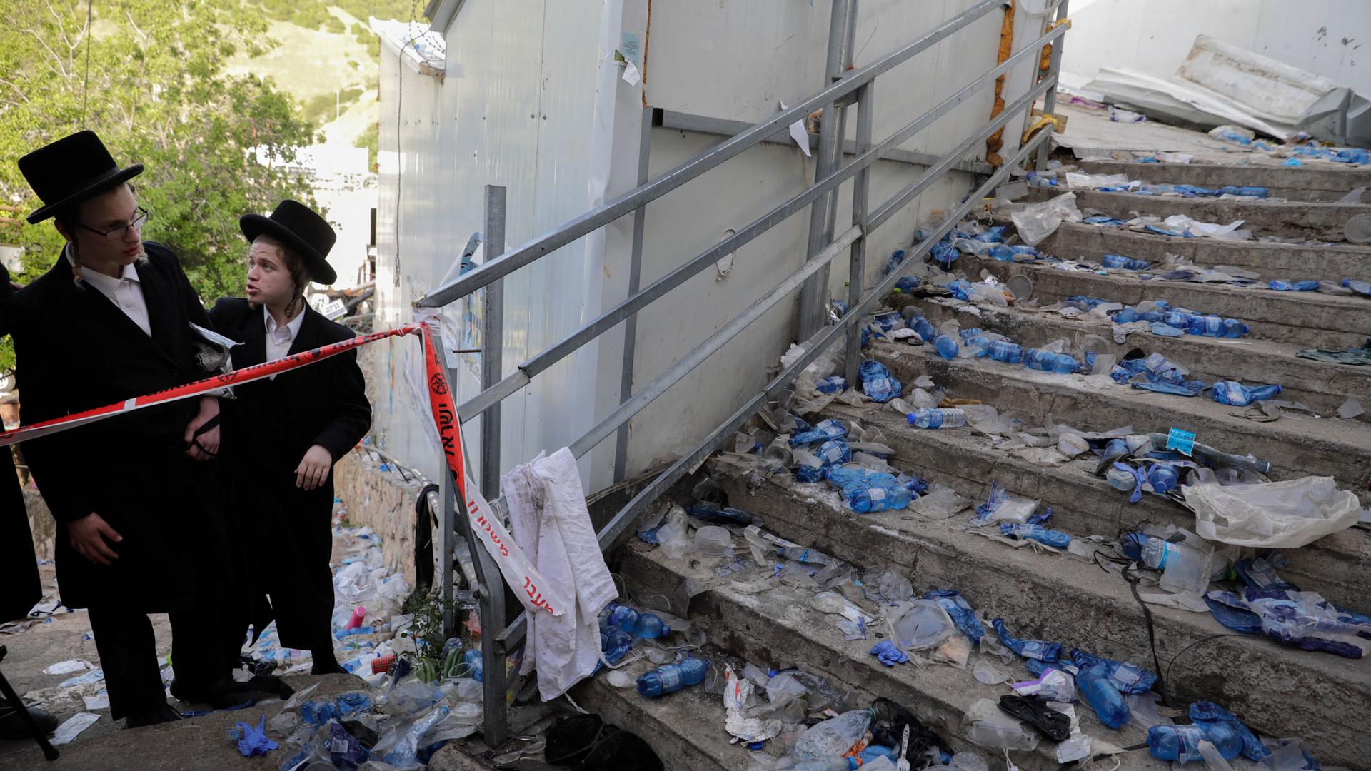Two young Jewish men are shown wearing Ultra Orthodox clothing and looking on to a staircase strewn with debris following a stampede.