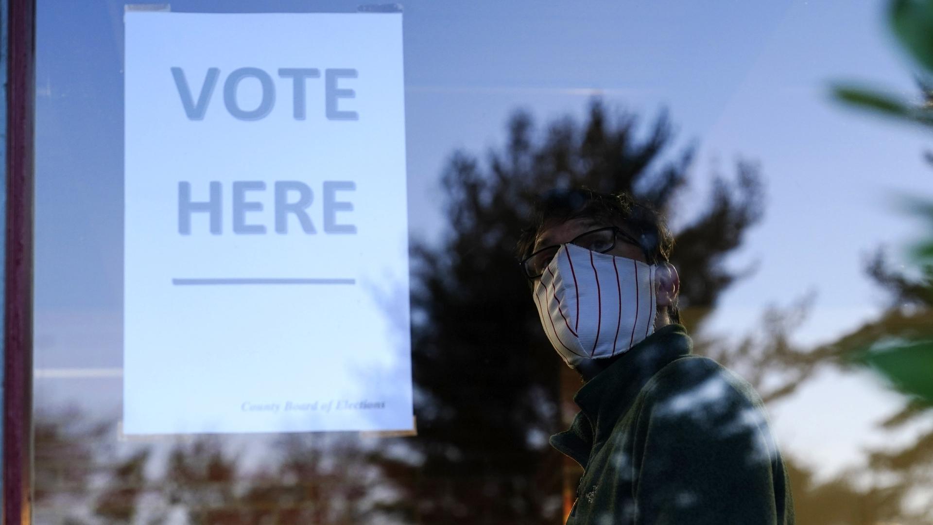 Vote sign in a window with masked man looking at it in reflection
