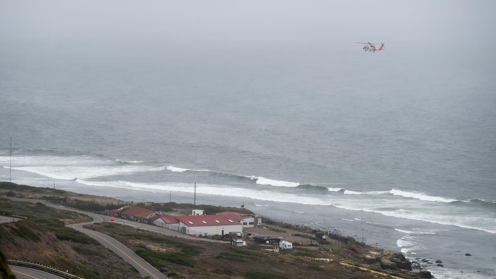 Waves are shown crashing into San Diego's coastline with a rescue helicopter flying above.