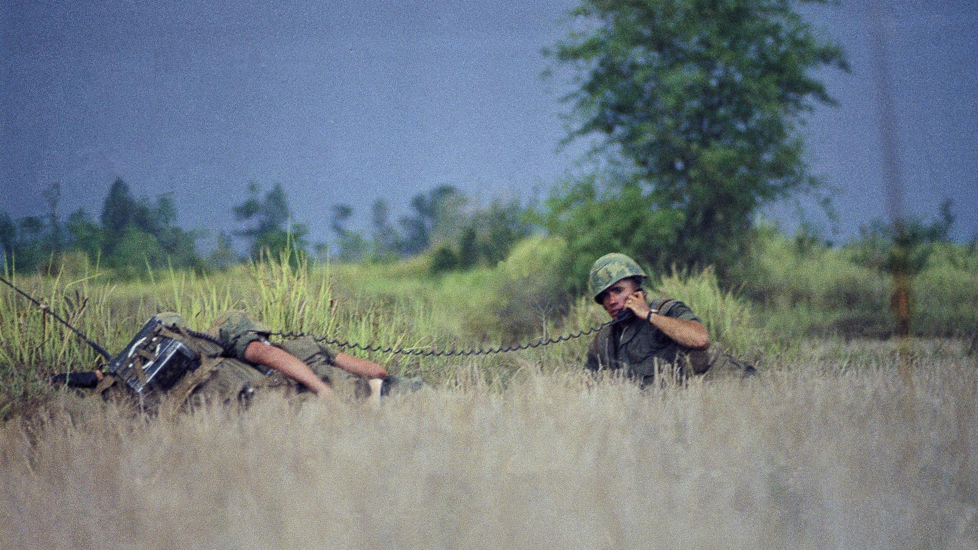 Two men in camouflage carry guns in a rice paddy in Vietnam. 