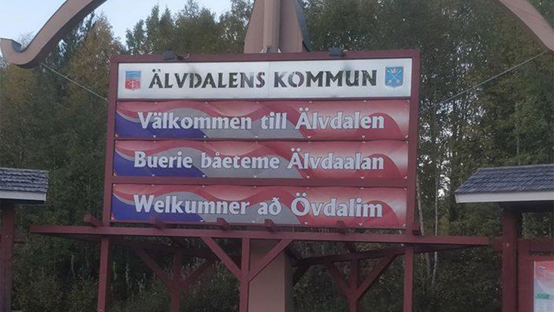 A red and white sign that says "Welcome to Älvdalen" in the language Elfdalian