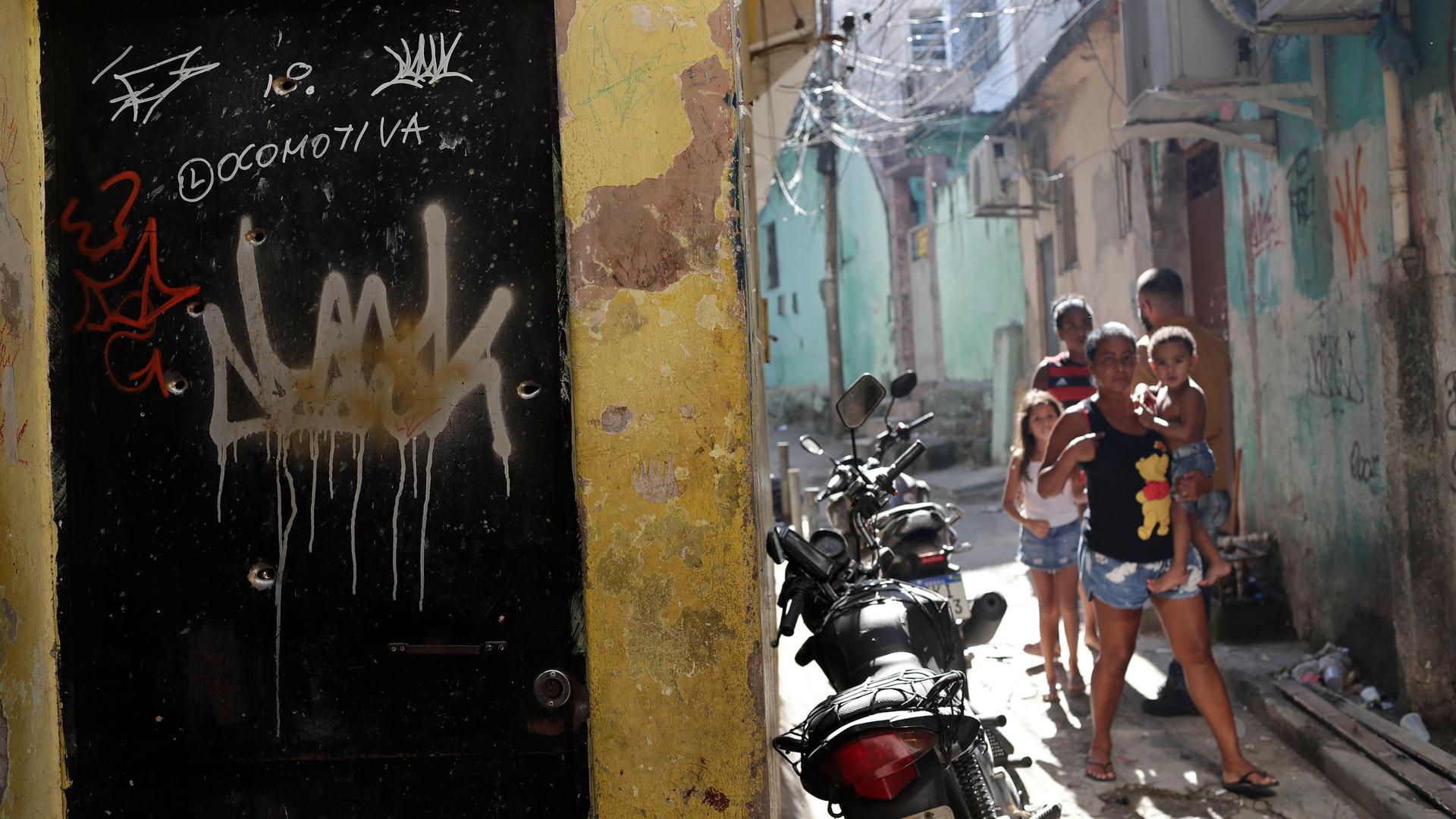 Residents walk near a doorway scared with bullet holes after a police raid against alleged drug traffickers in Rio de Janeiro, Brazil, May 6, 2021. 