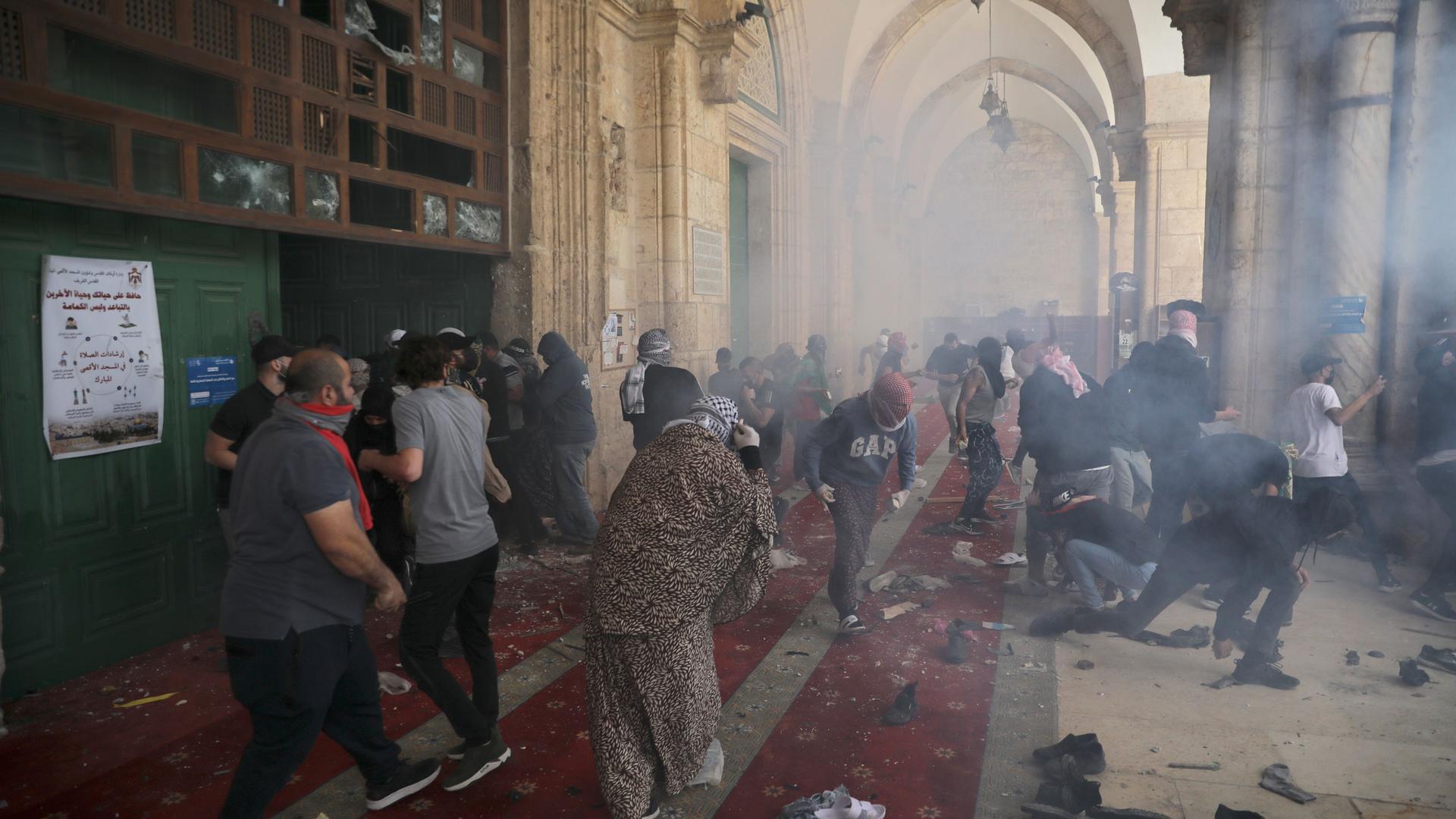 A large crowd of people are shown scattered in the Al-Aqsa Mosque as tear gas is shown surround the area.