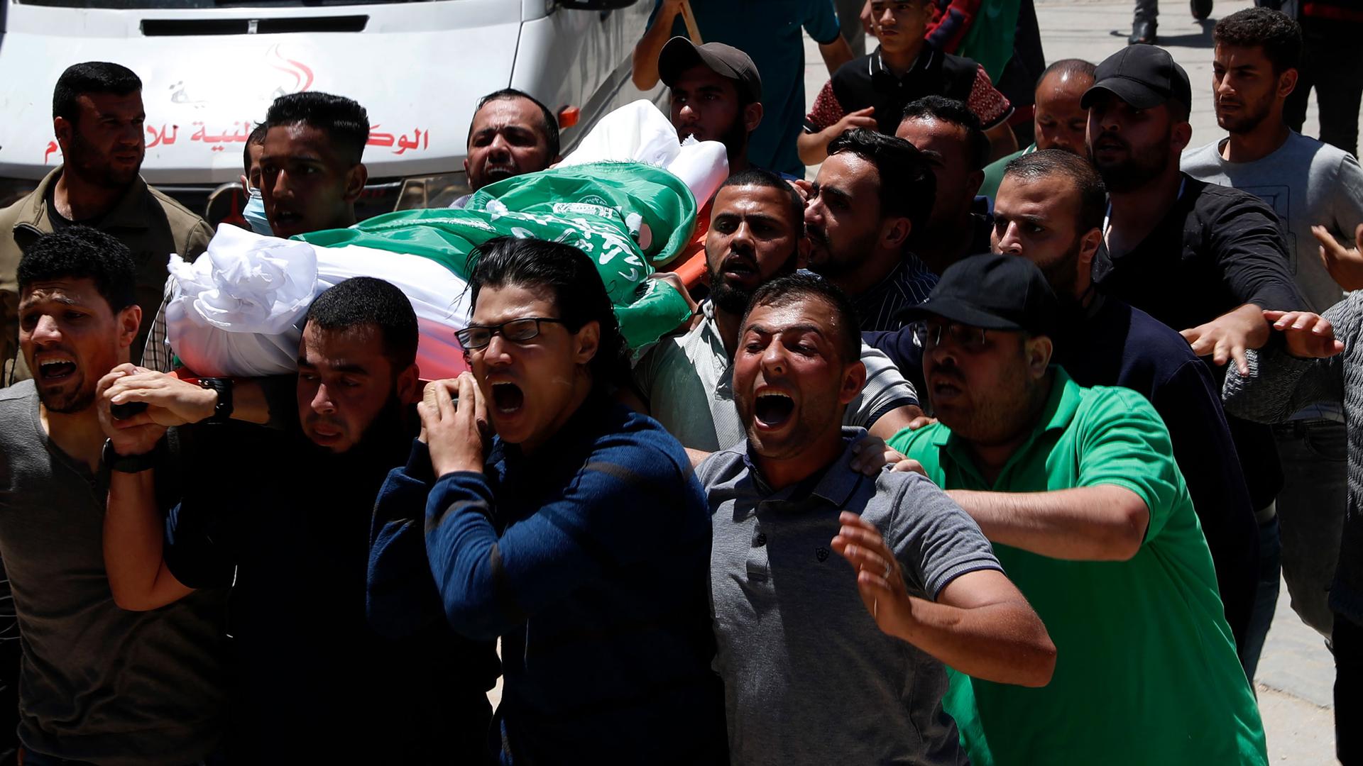 A group of people are shown carrying a body draped in white and the green flag of Hamas.