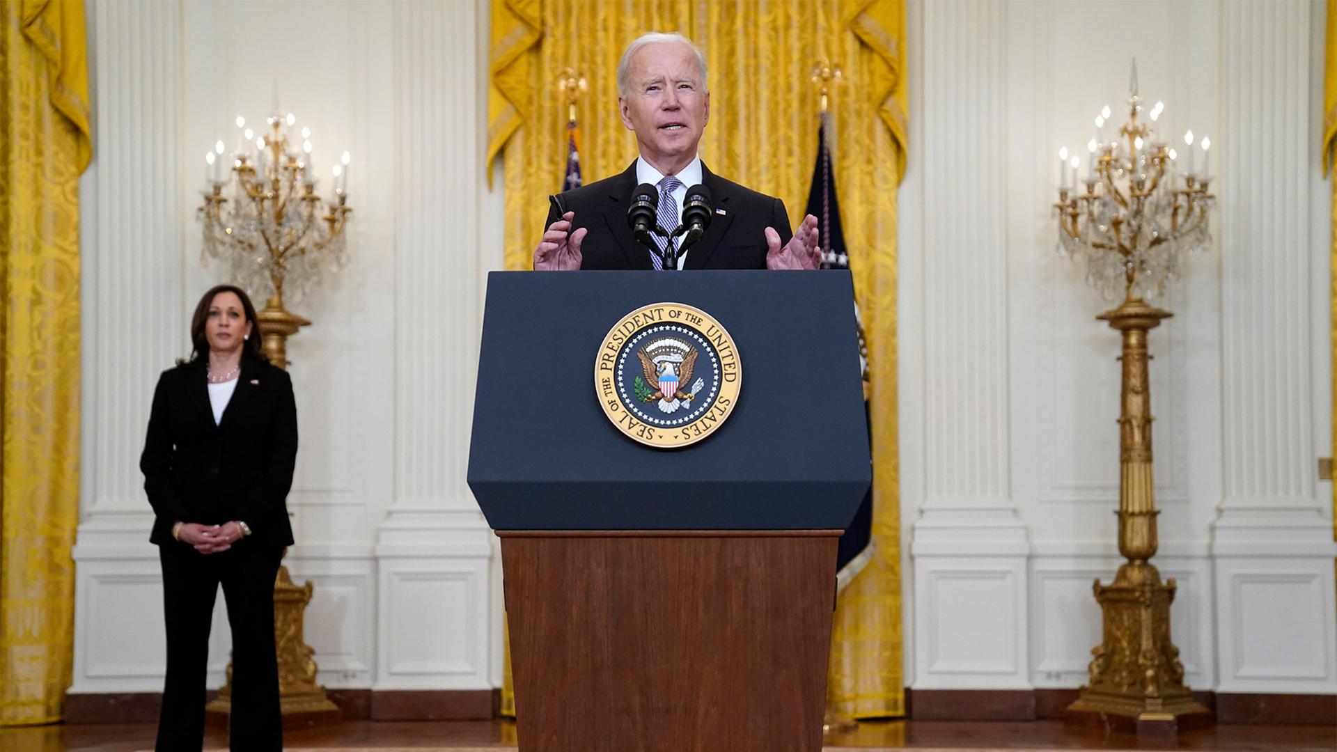 President Biden speaks at a podium while VP Harris stands to his right to listen