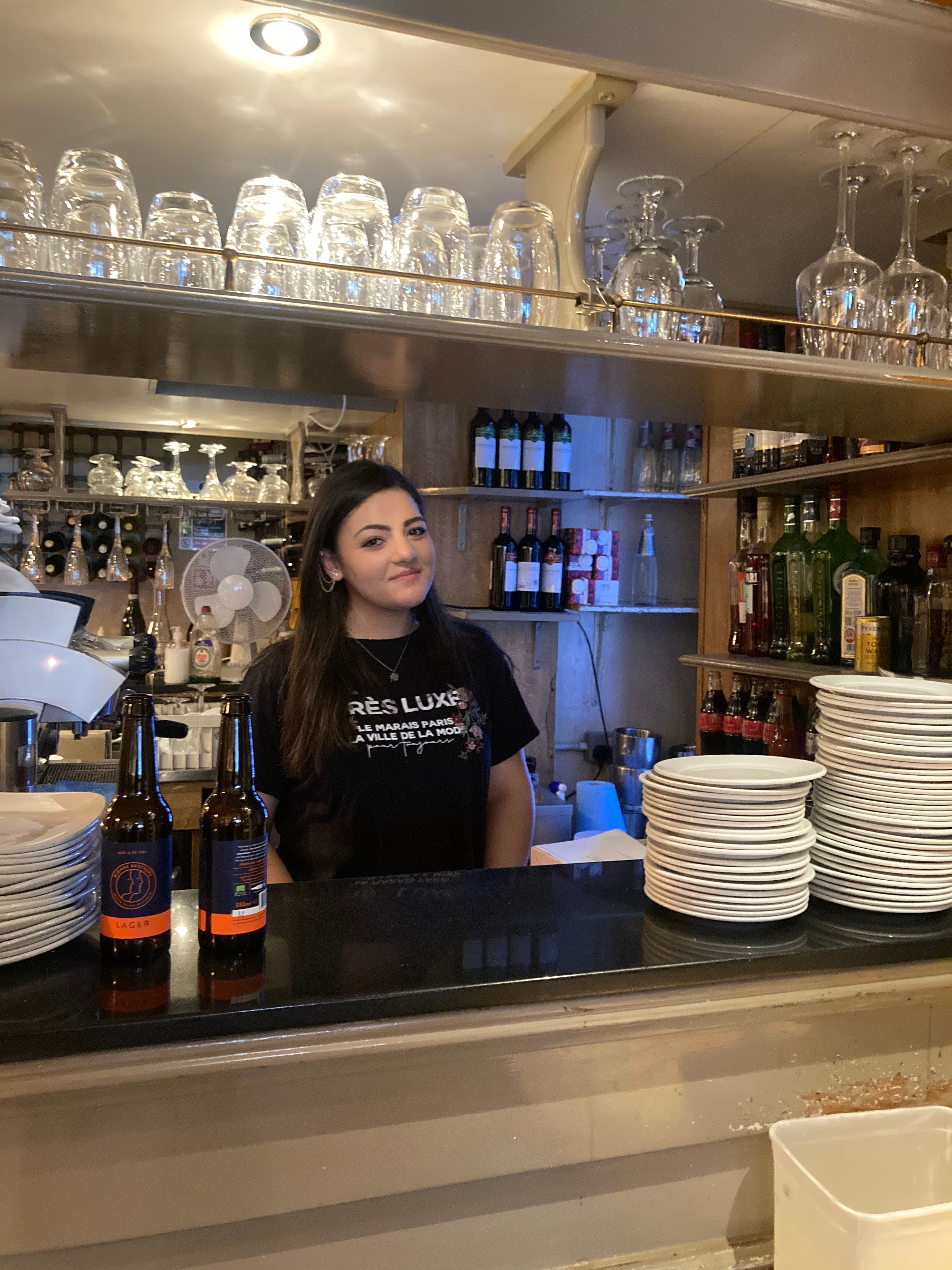 Giada Calabrese, from southern Italy, works behind the bar in a black shirt surrounded by cups and plates.