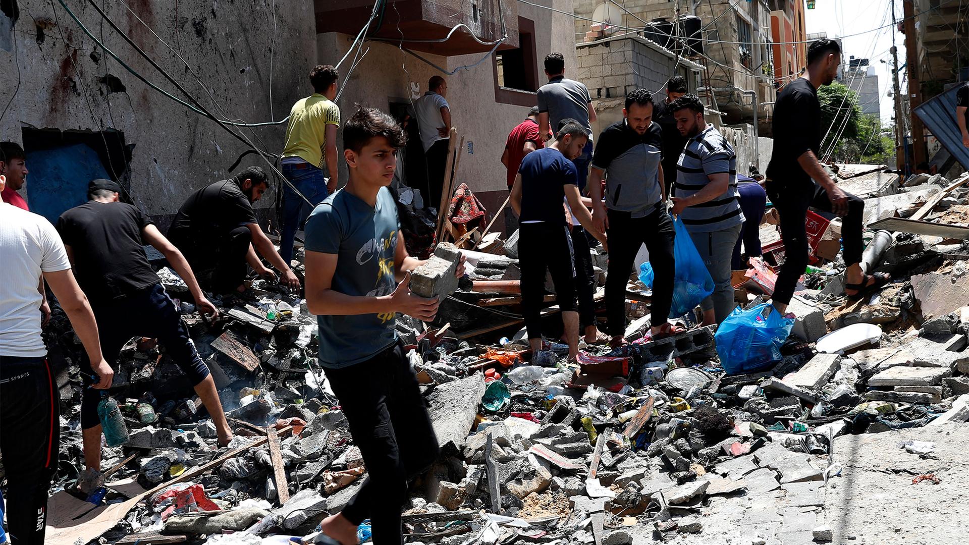 Young man in blue shirt lifts a piece of concrete as other men sift through rubble after an airstrike