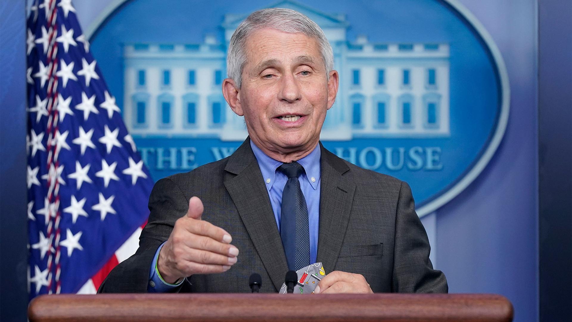 Dr. Fauci stands at a podium in the White House press room with the American flag over his shoulder