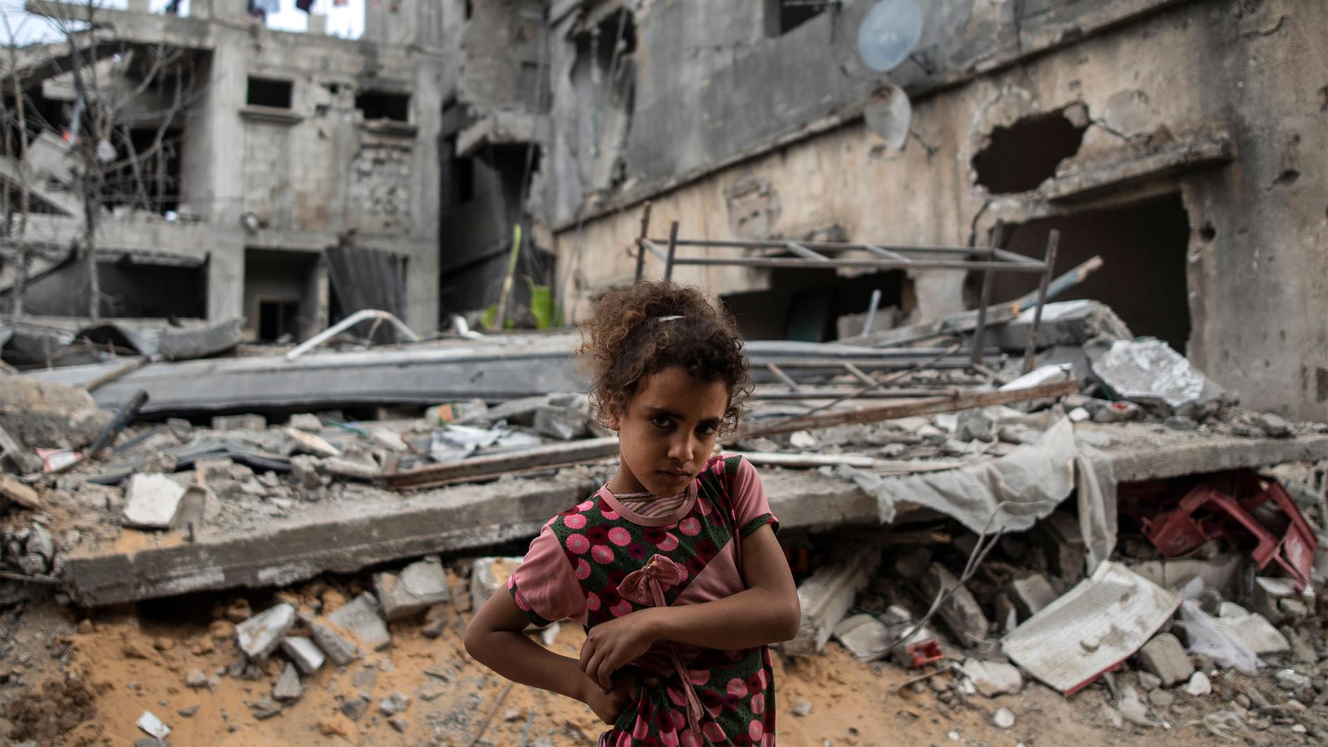 Girl stands in front of destroyed buildings