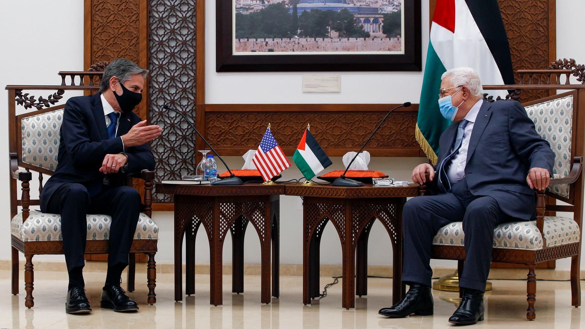 Palestinian President Mahmoud Abbas and US Secretary of State Antony Blinken are show sitting in opposite armchairs with two wooden side tables between them.