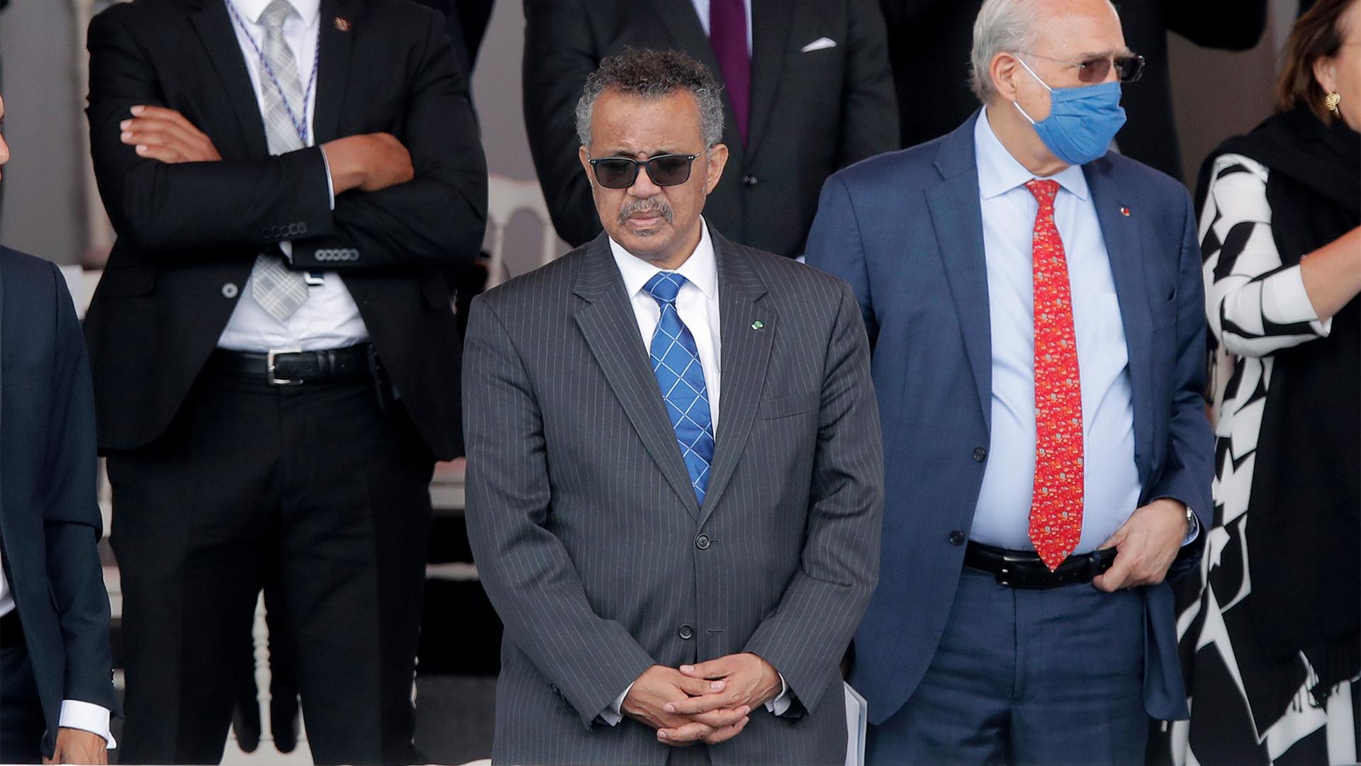Men in suits, some wearing masks and sunglasses stand together