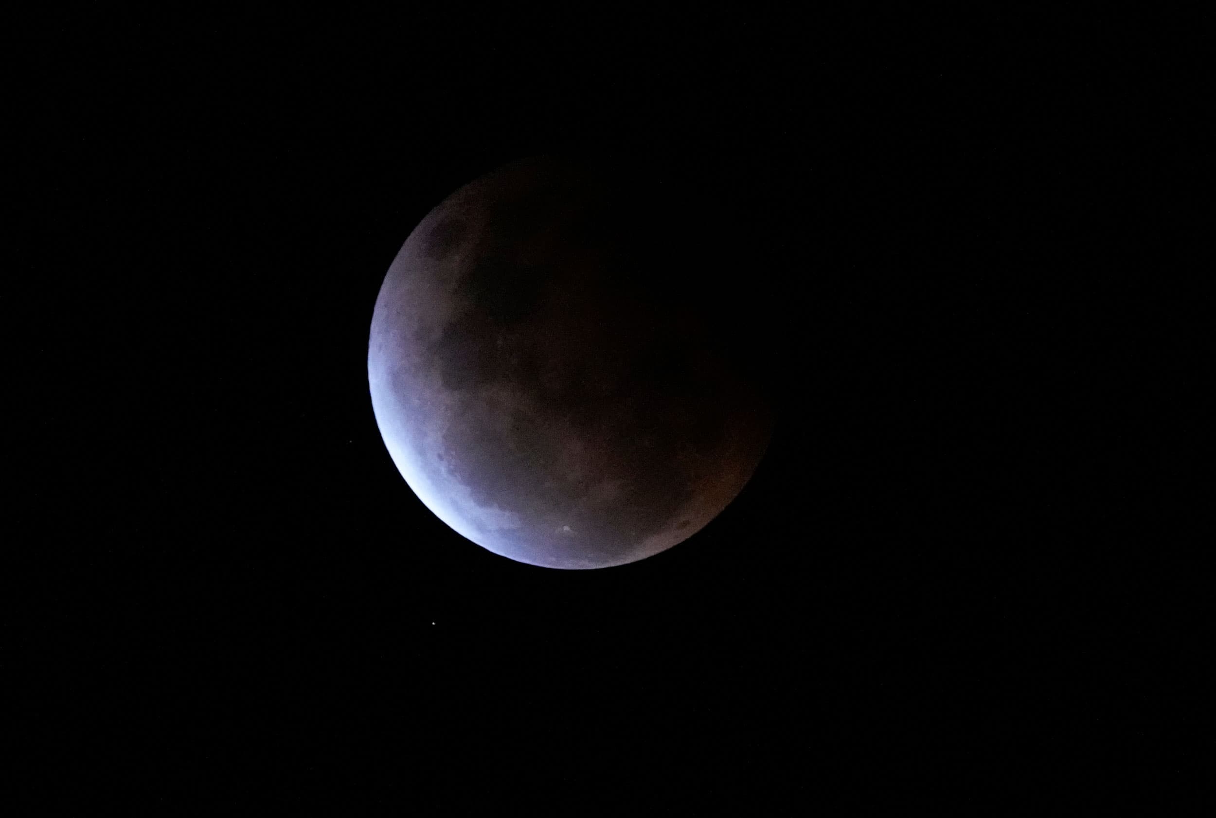Earth's shadow continues across the full moon nearly covering the entire surface before the orange colors from the sun appear.