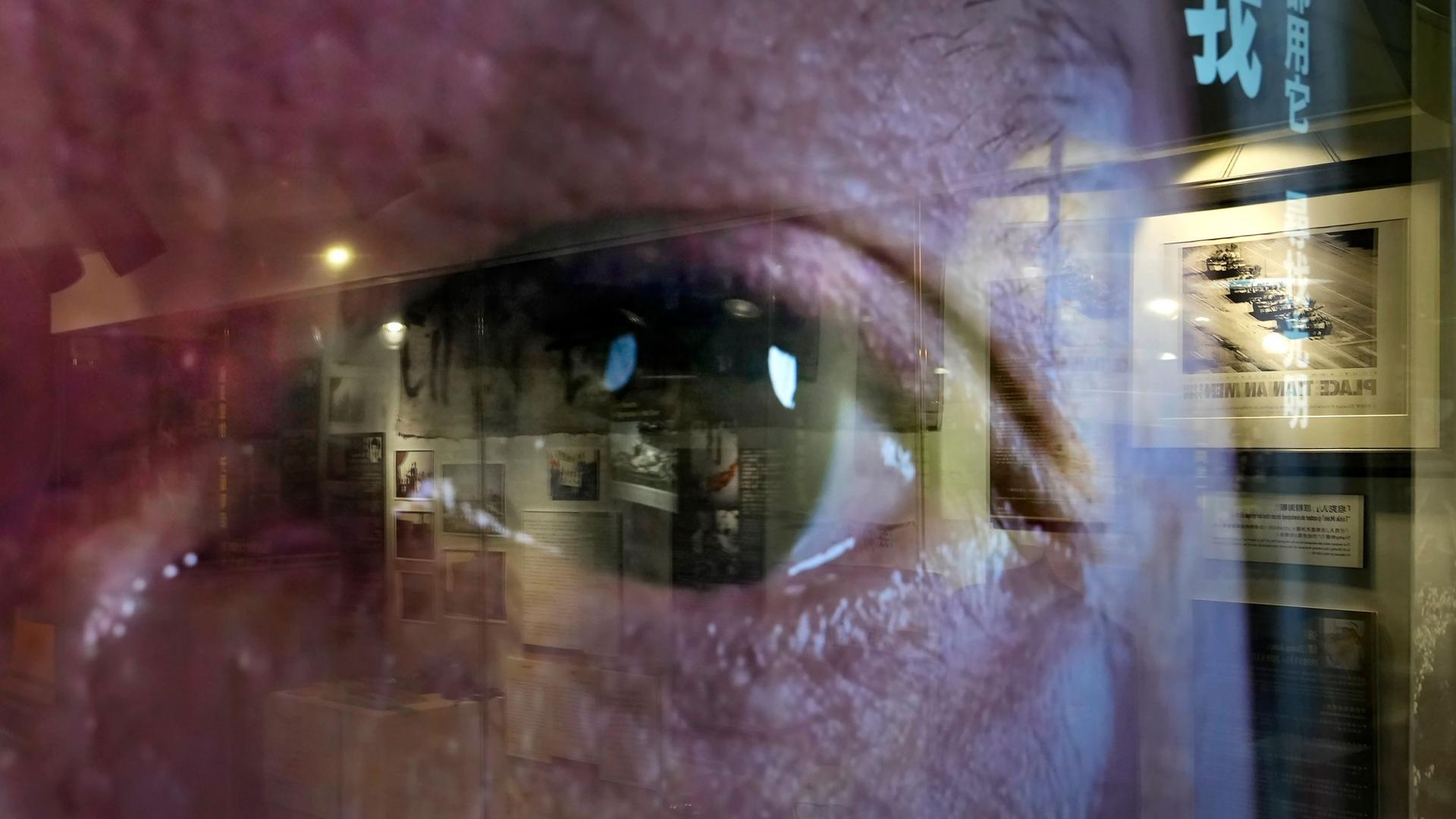 A close of photograph showing a person's eye and seen through clear glass reflecting the image of a gallery exhibit.