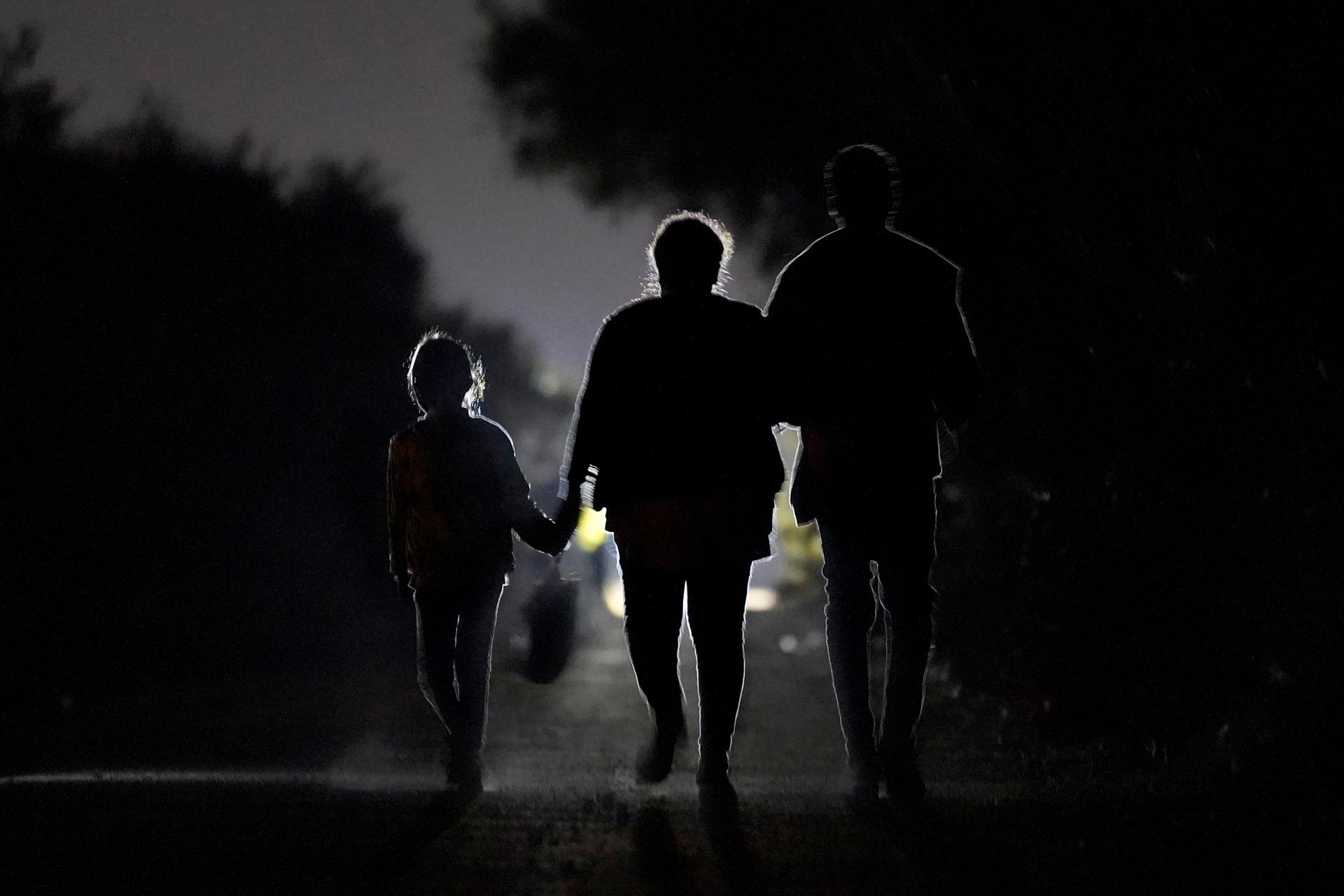Figures of a 7-year-old migrant girl walking with a woman and unidentified man silhouetted at night