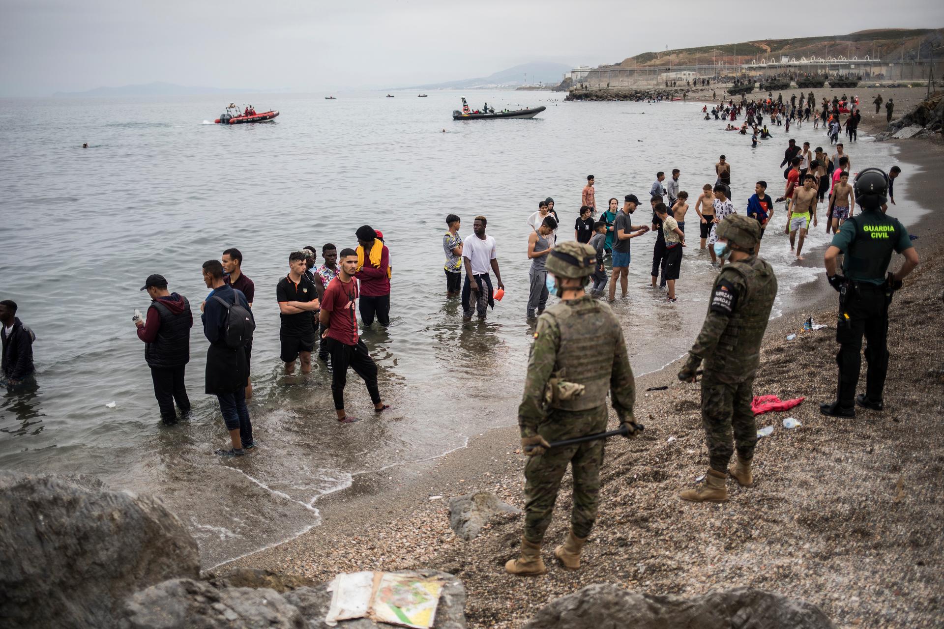 People mainly from Morocco stand on the shore as the Spanish Army cordons off the area at the border of Morocco and Spain, at the Spanish enclave of Ceuta, May 18, 2021. 