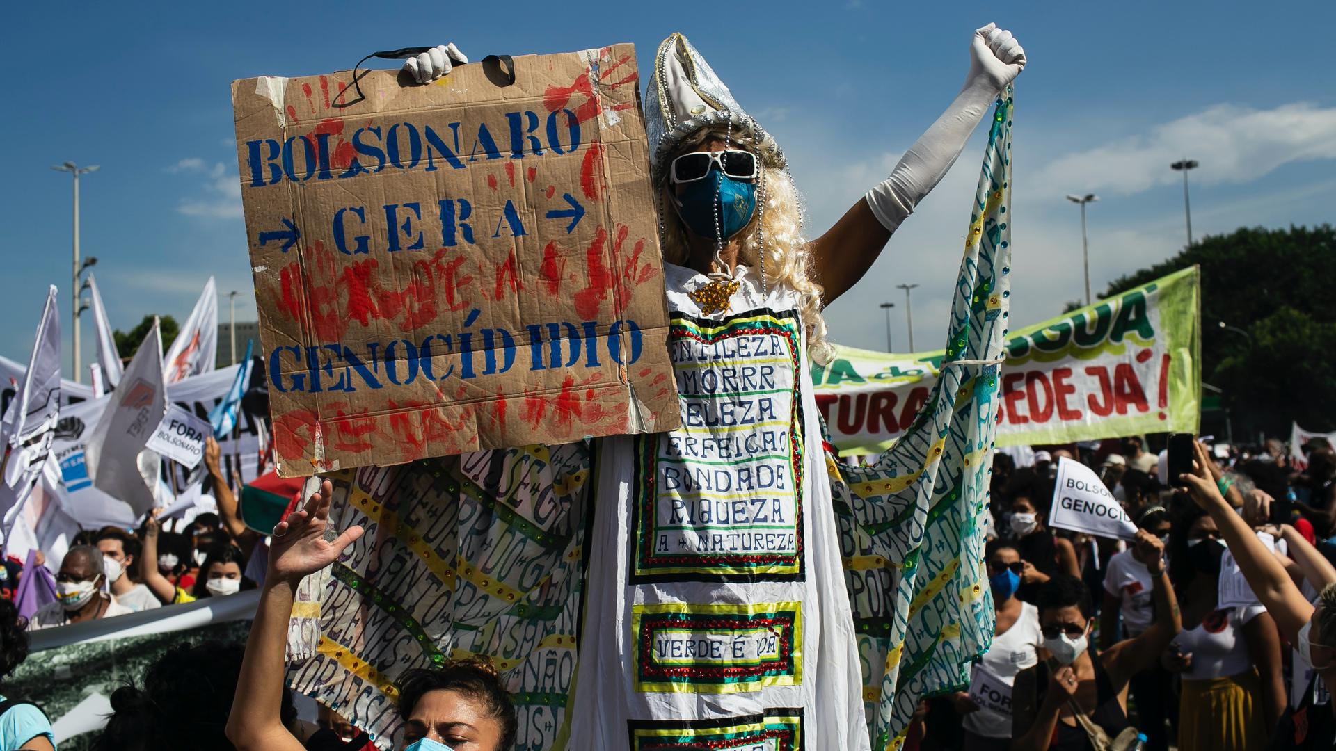 A man walking on stilts holds a sign with a message that reads in Portuguese: "Bolsonaro generates genocide"
