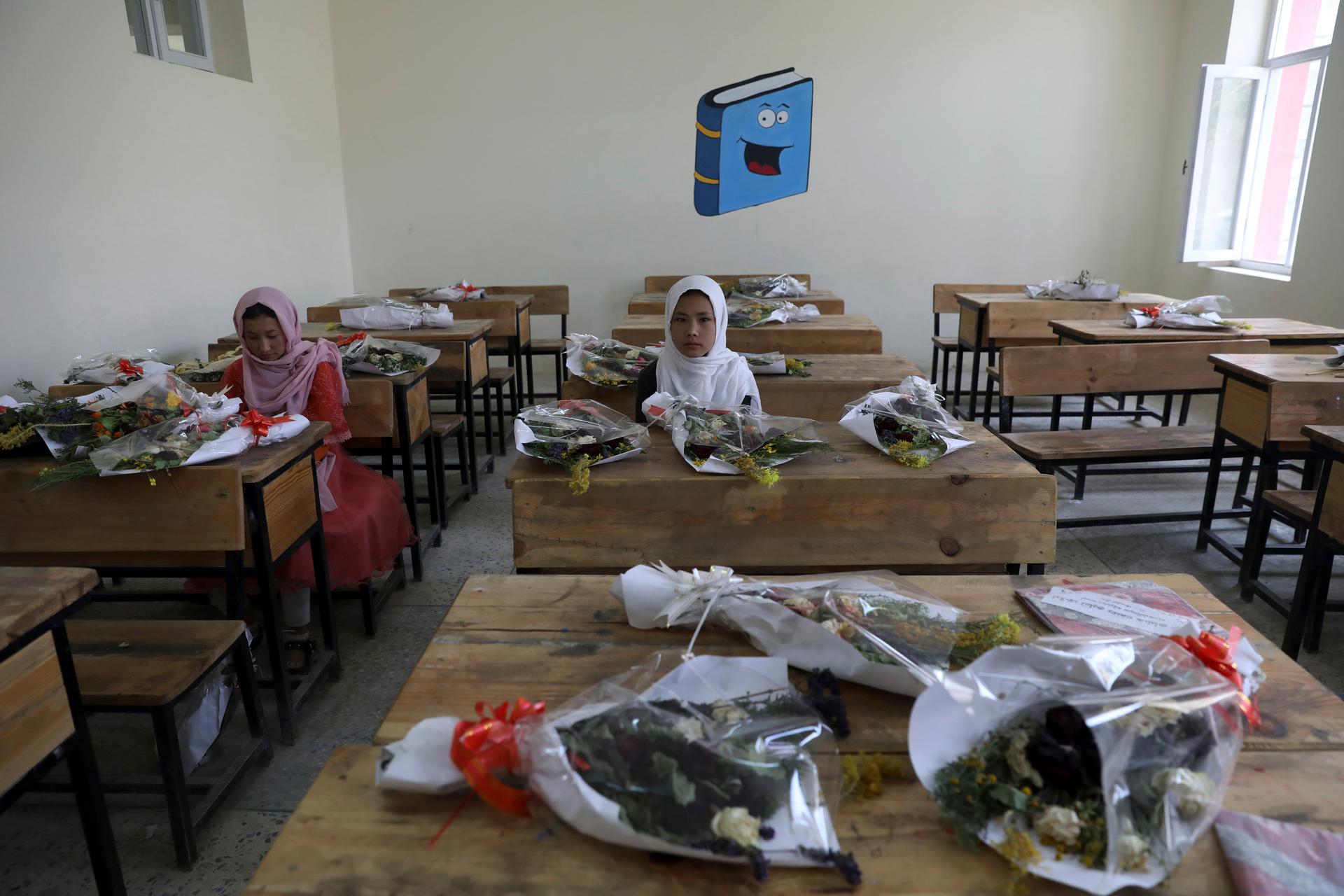 Schoolgirls sit inside a classroom with bouquets of flowers on empty desks in Afghanistan