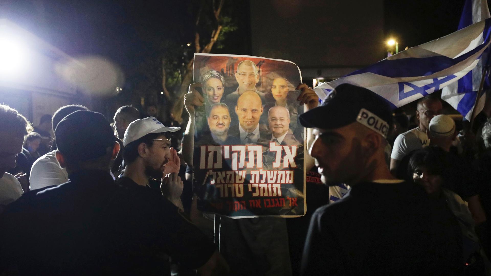 Israeli police officers stand guard as right-wing protesters chant slogans and hold signs.