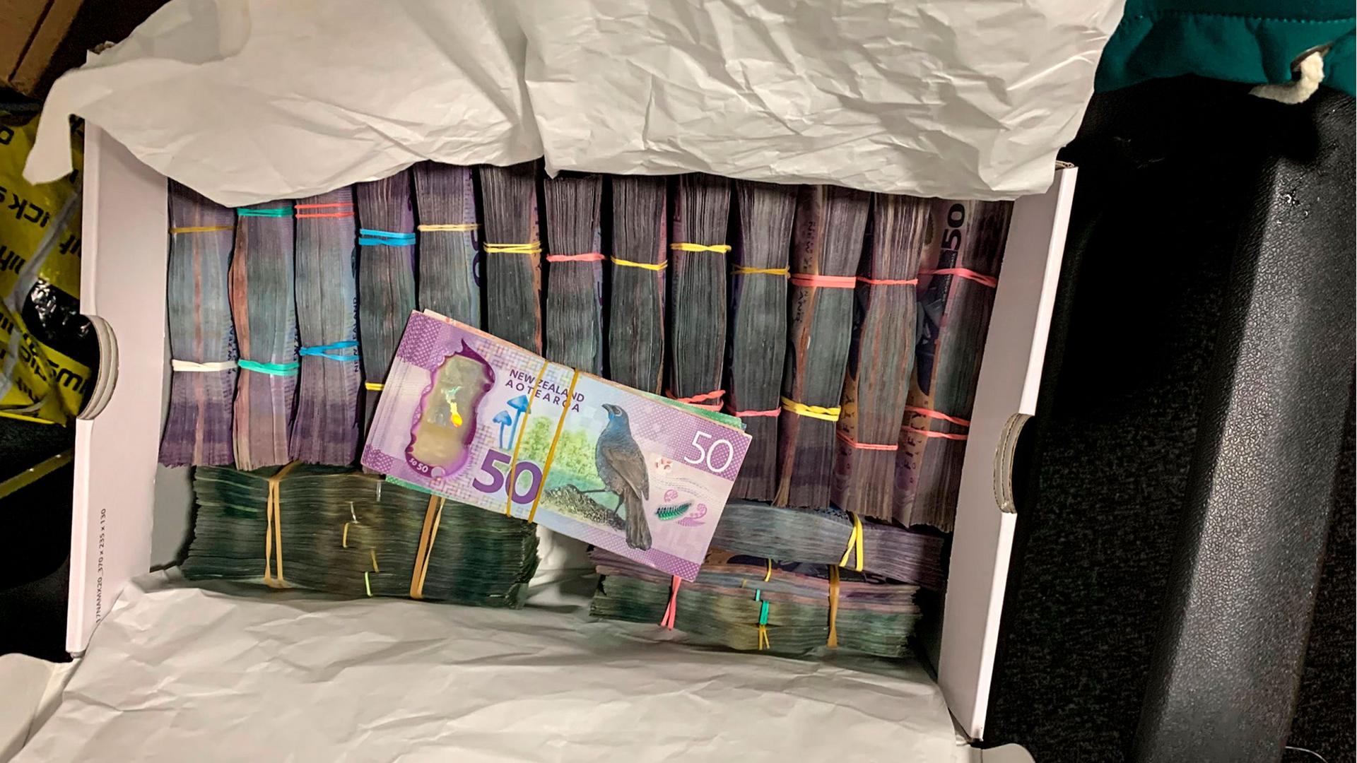 A box containing stacks of cash with a 50 note stack from New Zealand on top