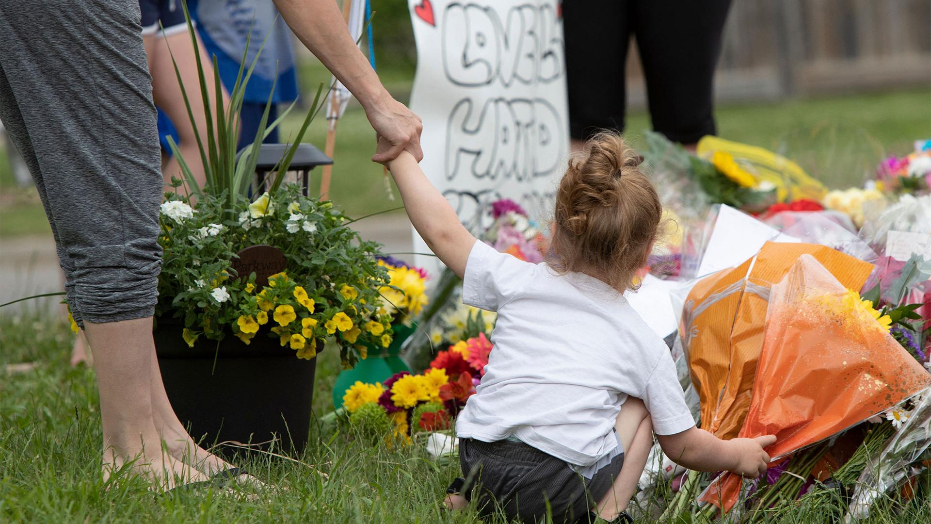 A woman holds on to a child's hand and she places flowers at a memorial