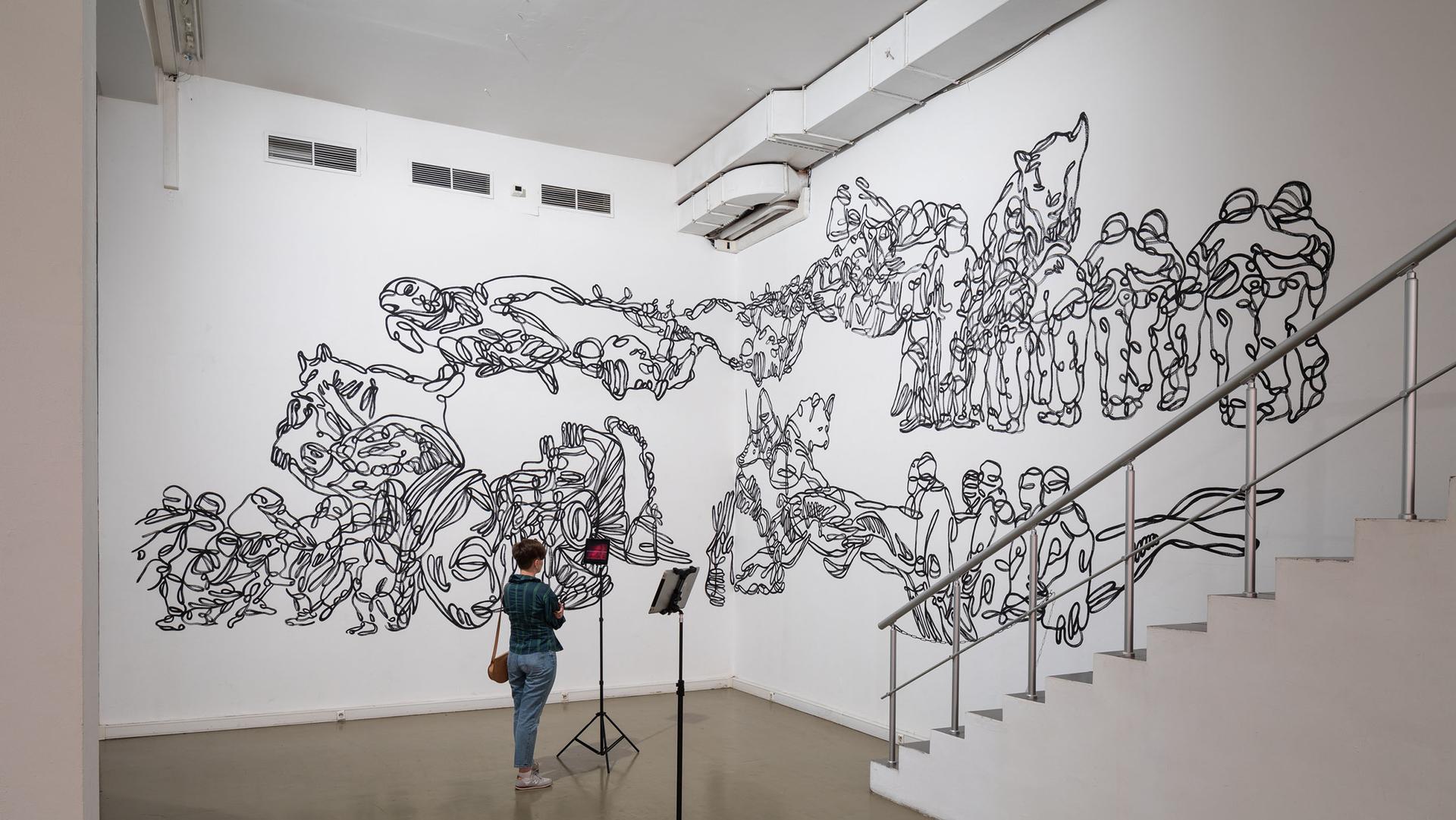 A white wall with black ink drawings and a person standing to view it