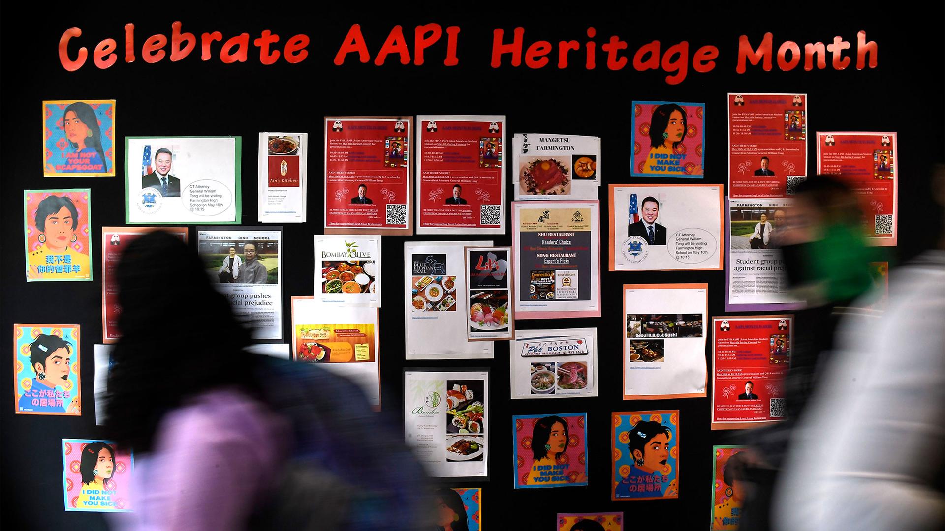 People walk past a board full of pictures celebrating AAPI heritage month
